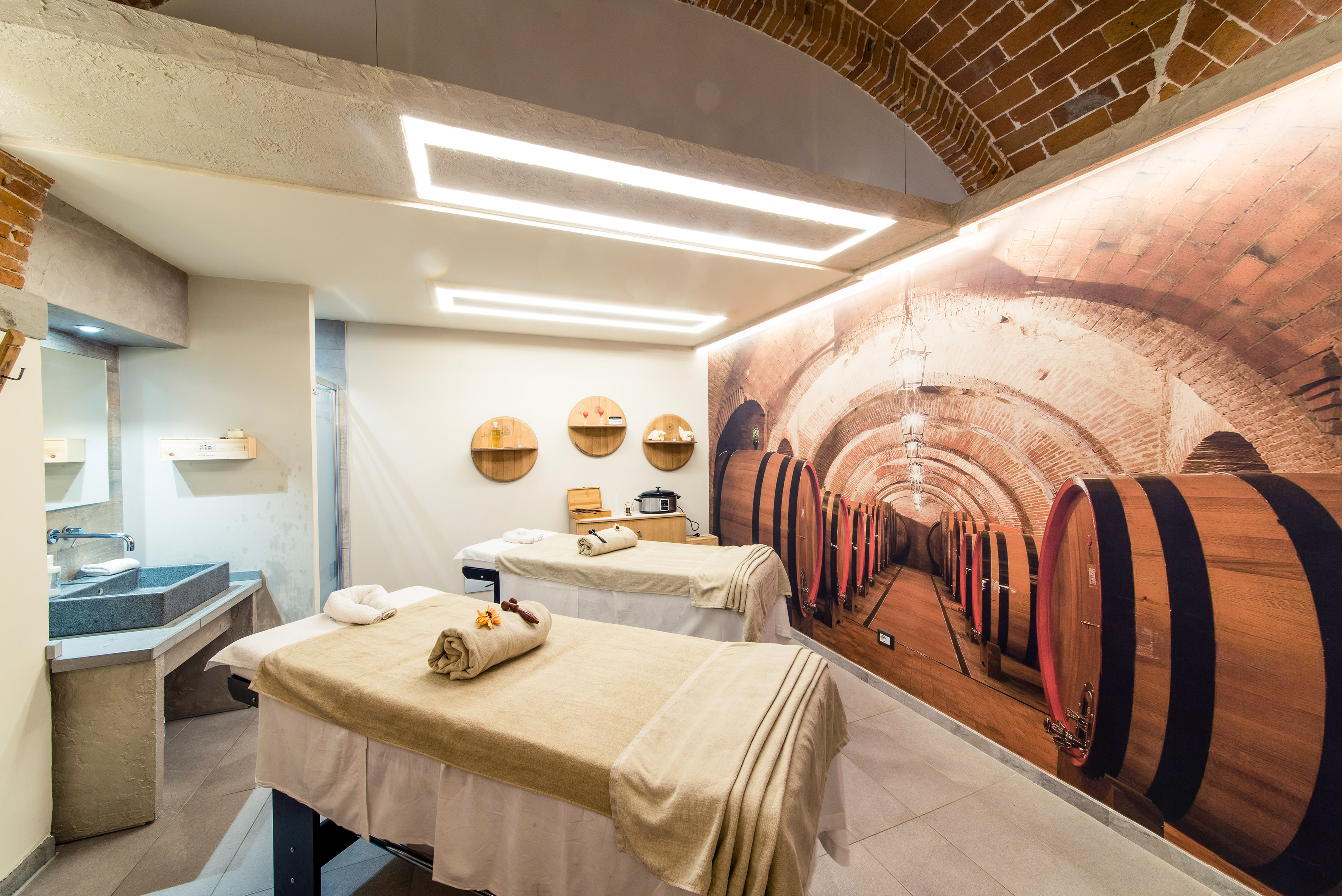 Wellness spa room with two massage beds, stone sink, and wine cellar mural.