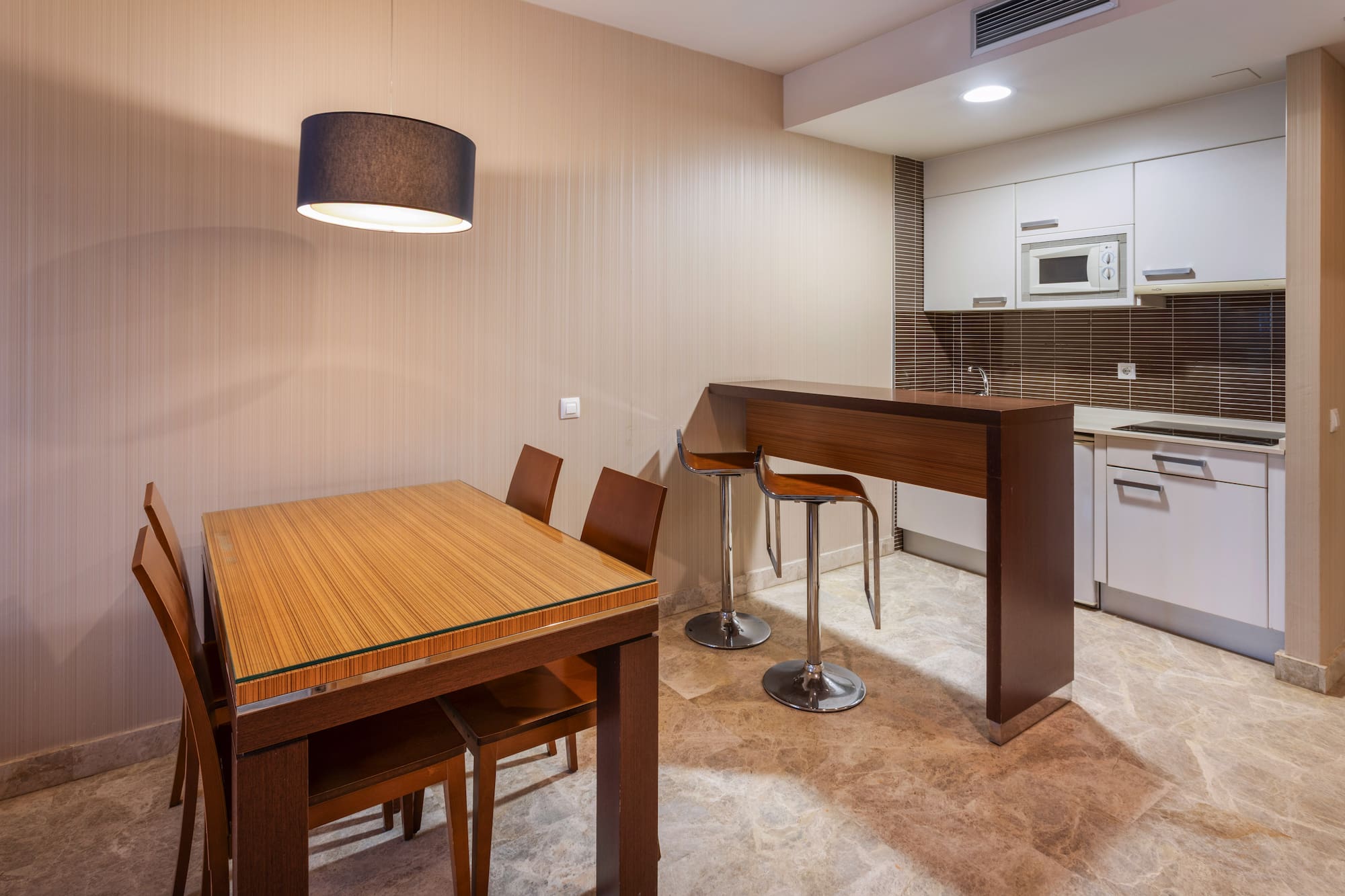 Modern dining kitchen with wood table, bar stools, white cabinets, and stone floor.