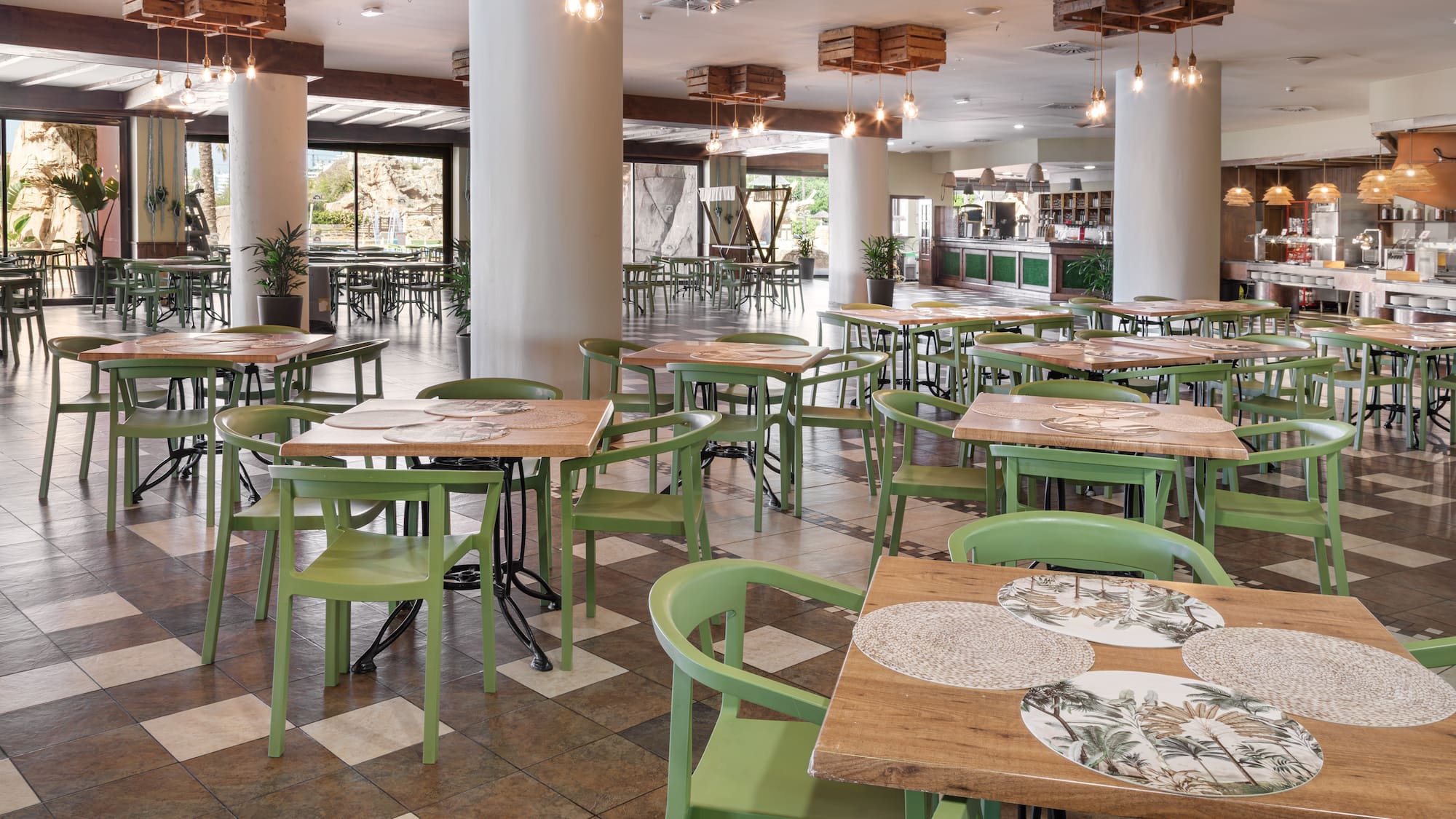 Spacious hotel restaurant with green chairs, wooden tables, and buffet area.
