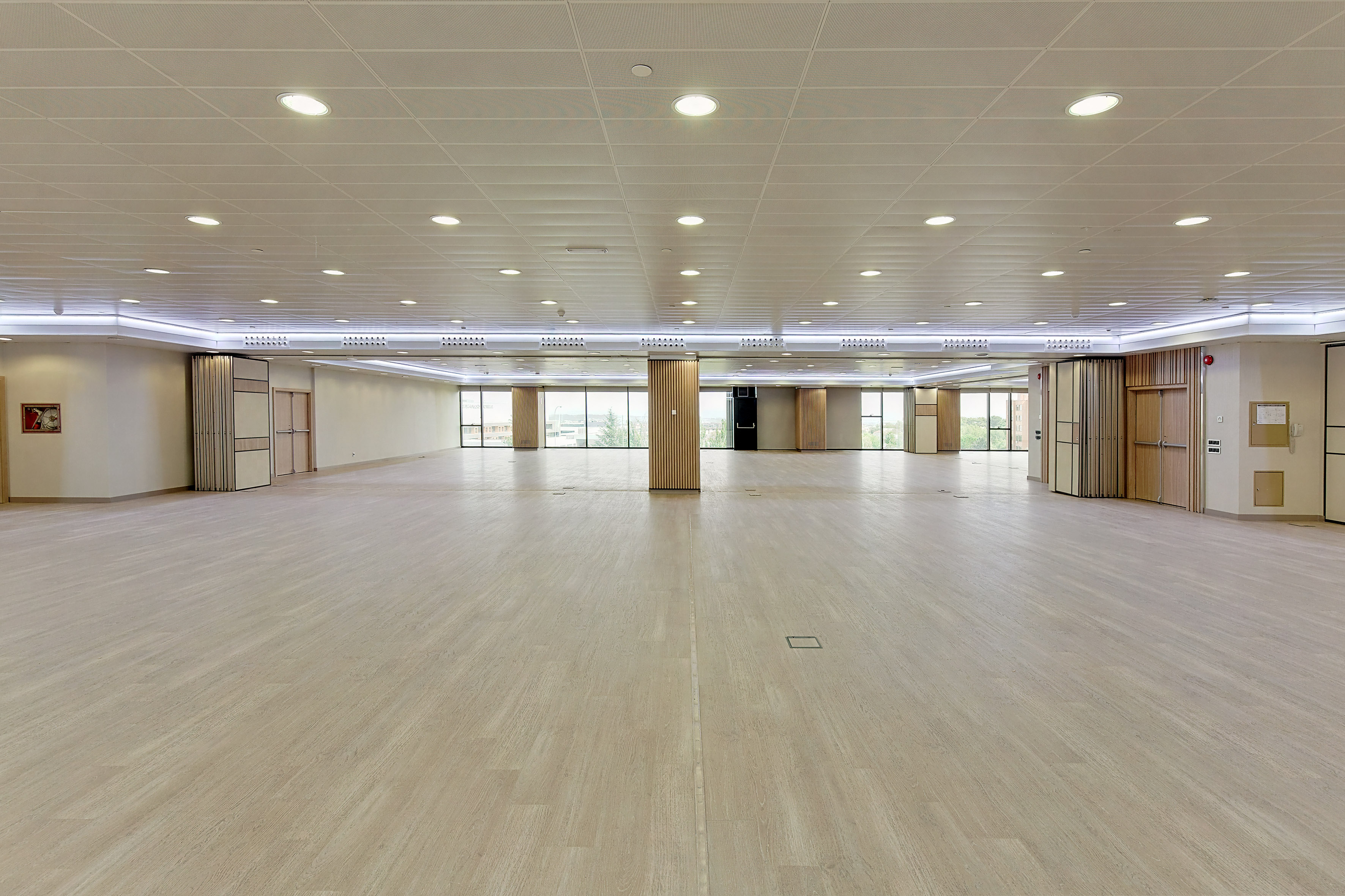 Empty modern event hall with light wood floor, windows, and flexible partition walls.