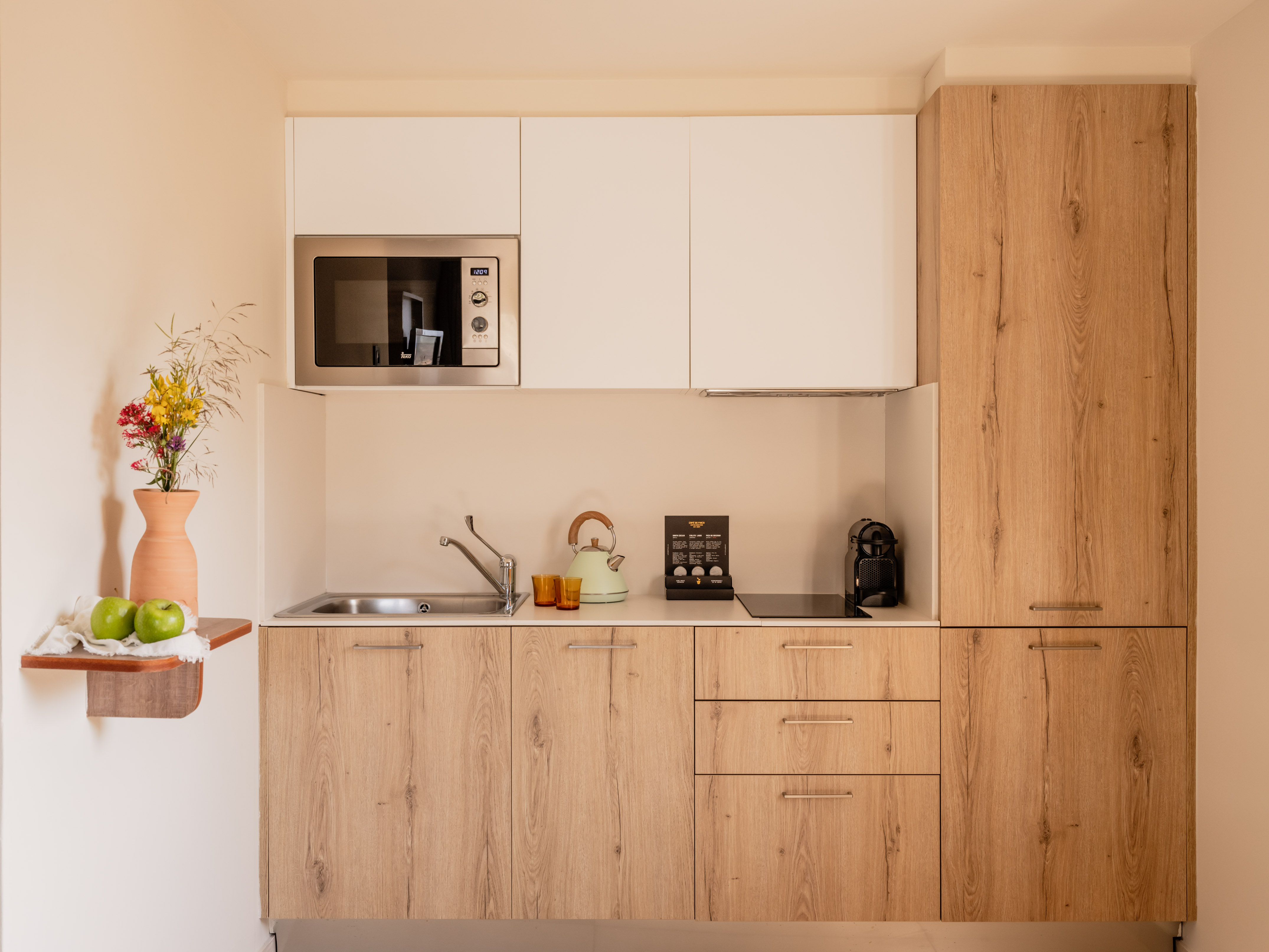 Modern kitchenette with wood and white cabinets, microwave, and sink.