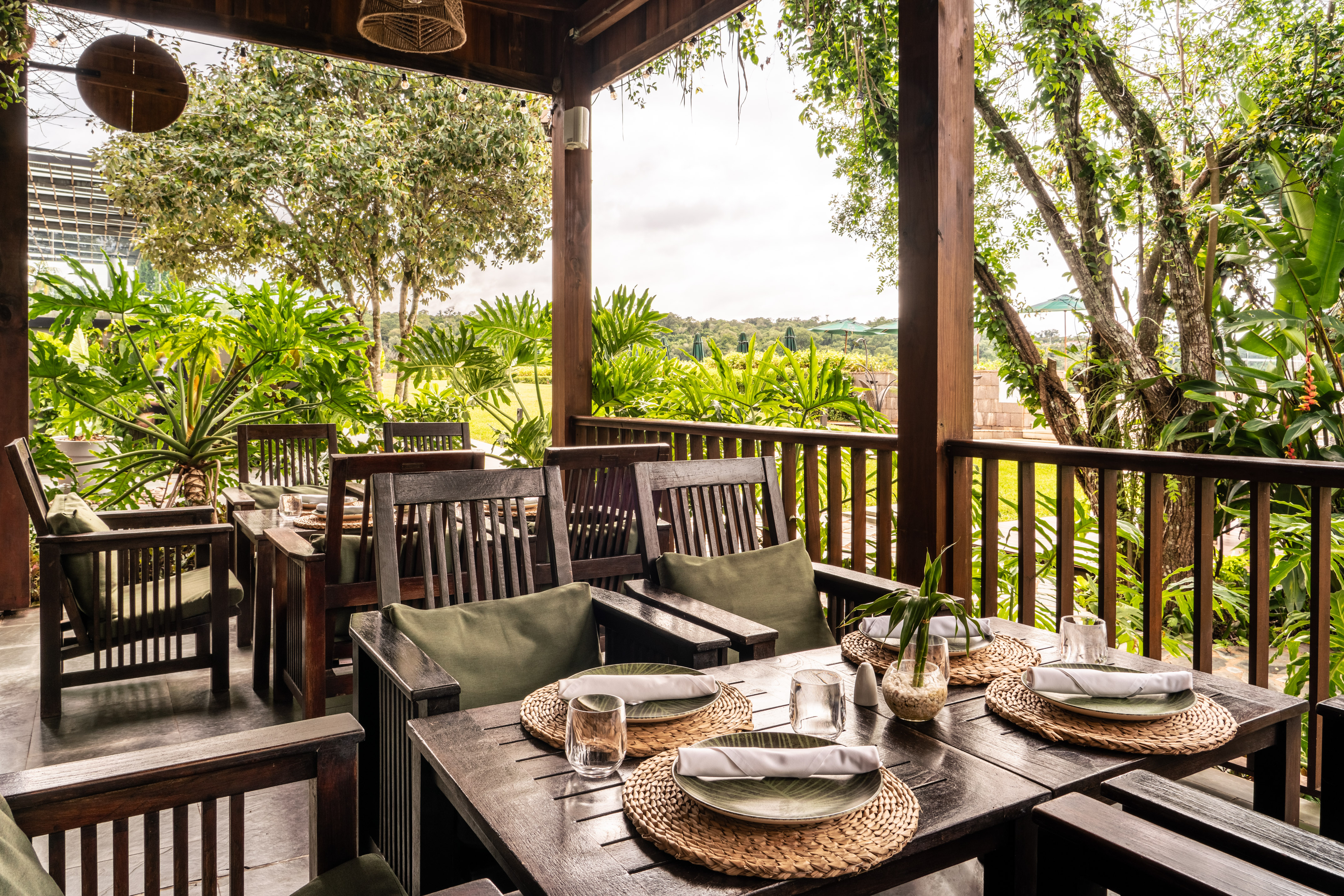 Tropical outdoor restaurant patio with set wooden tables and lush plants.