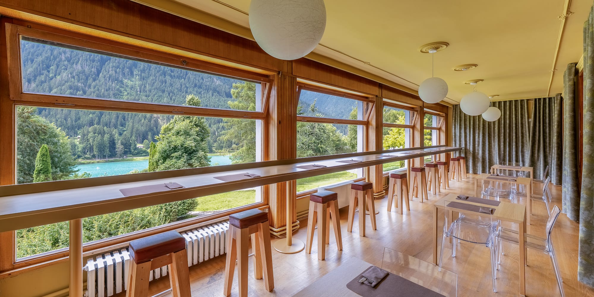 Panoramic lake and mountain view from a restaurant with window bar seating.