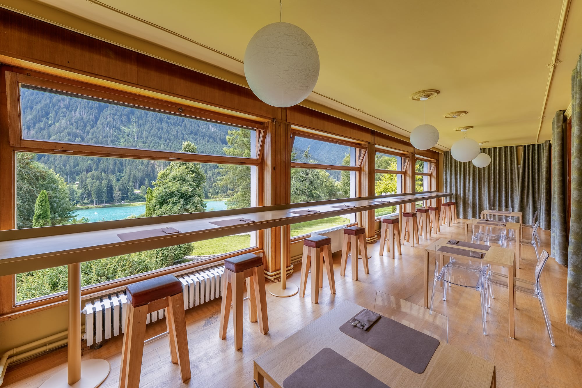 Panoramic lake and mountain view from a restaurant with window bar seating.