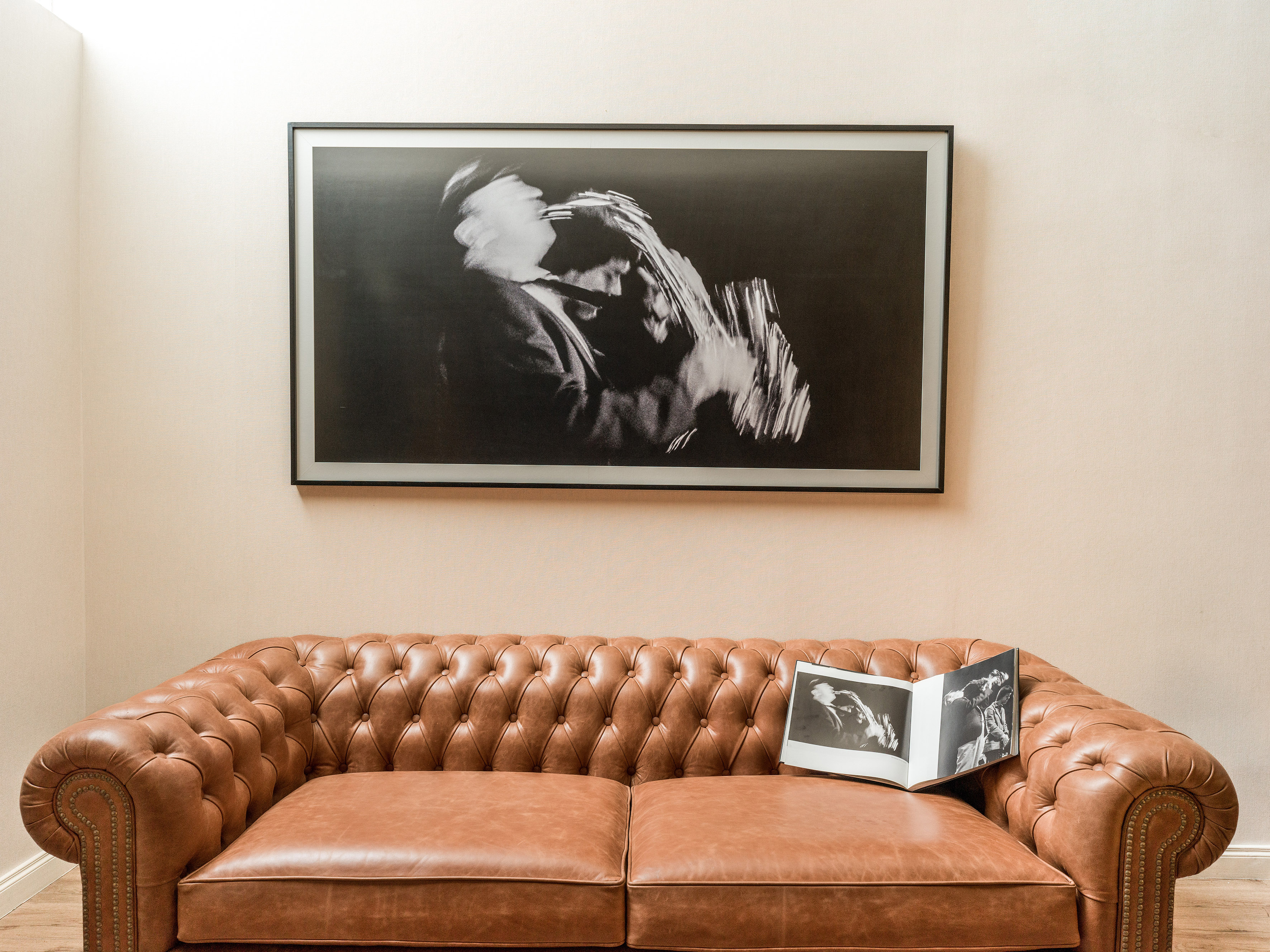 Brown leather Chesterfield sofa, framed B&W music photo, open book on cushion.
