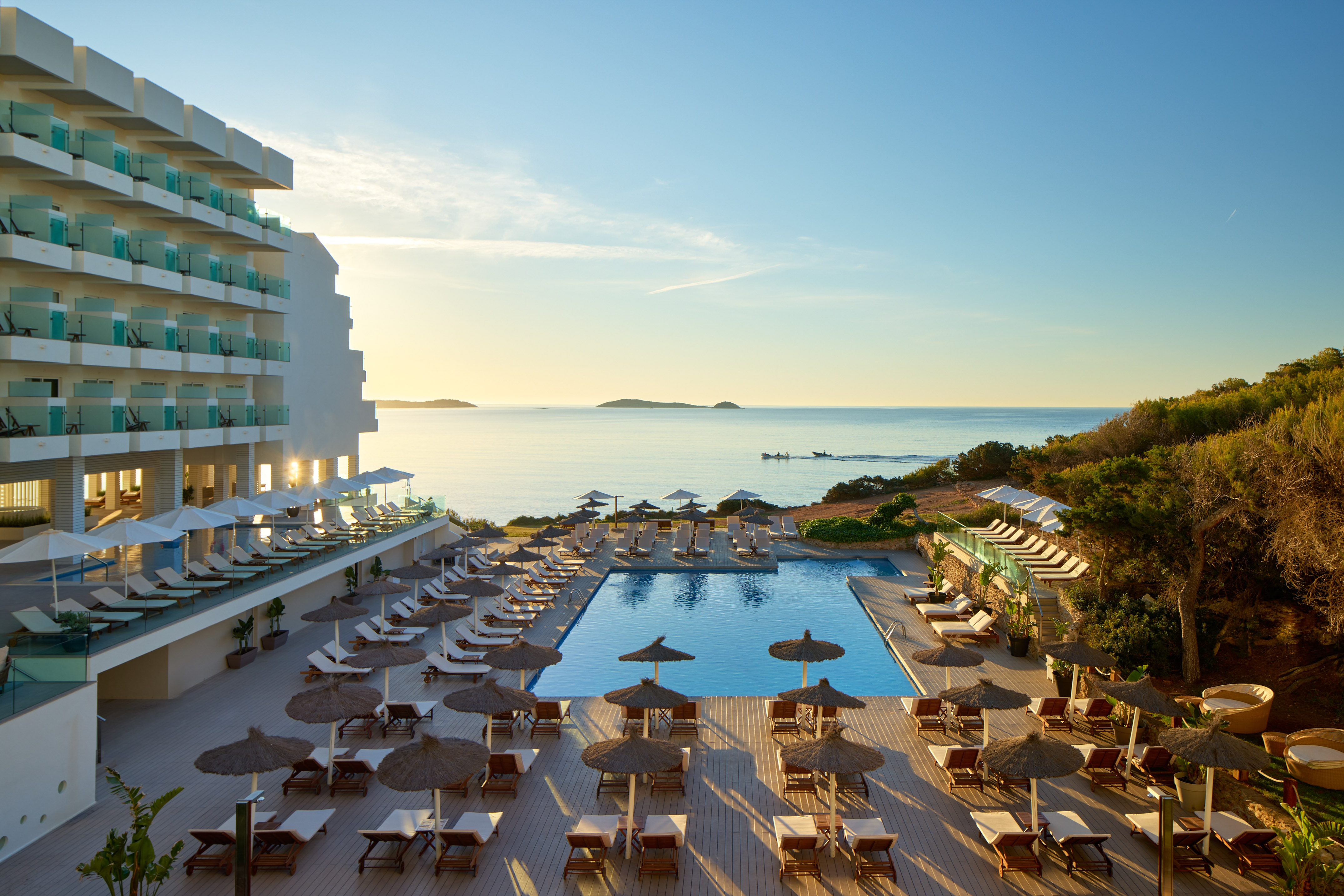 Oceanfront luxury resort with large pool, sun loungers, and beautiful sunset.