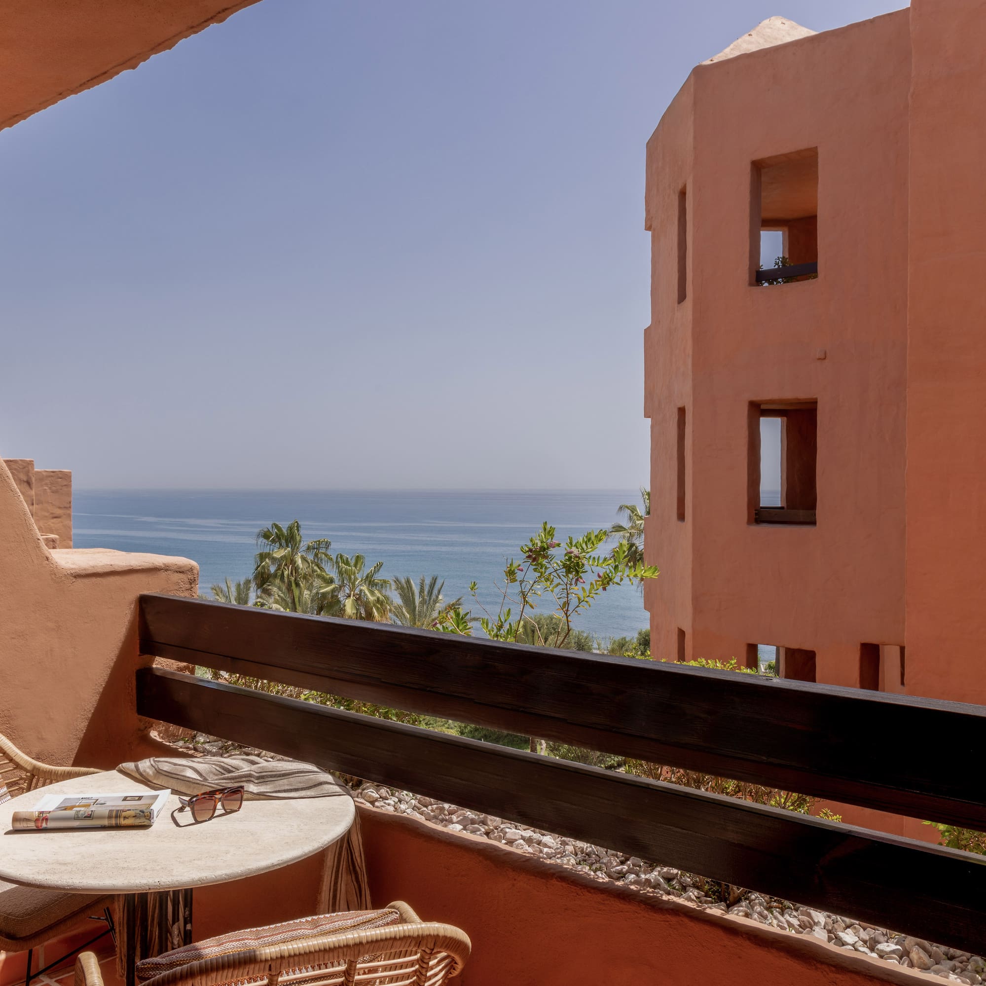 Terracotta balcony with ocean view, rattan furniture, and resort building.