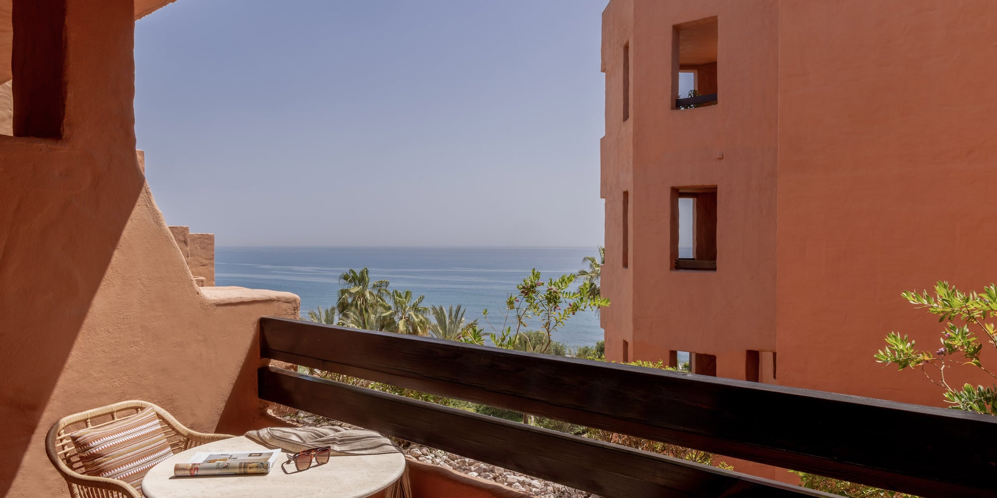 Terracotta balcony with ocean view, rattan furniture, and resort building.