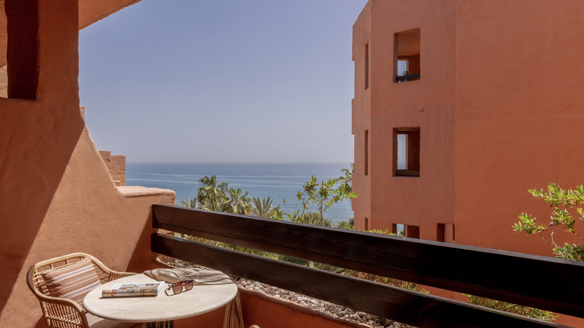 Terracotta balcony with ocean view, rattan furniture, and resort building.