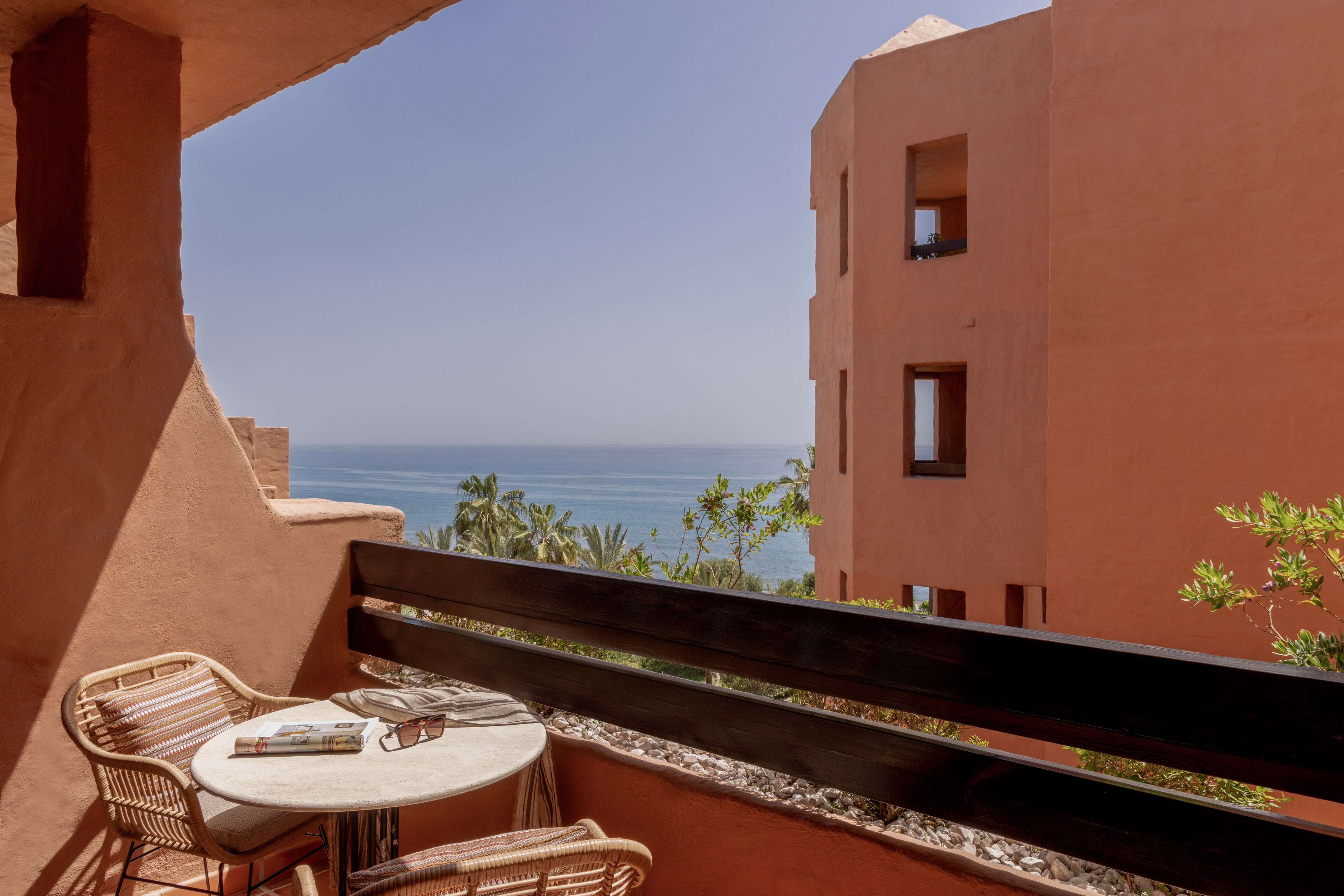 Terracotta balcony with ocean view, rattan furniture, and resort building.