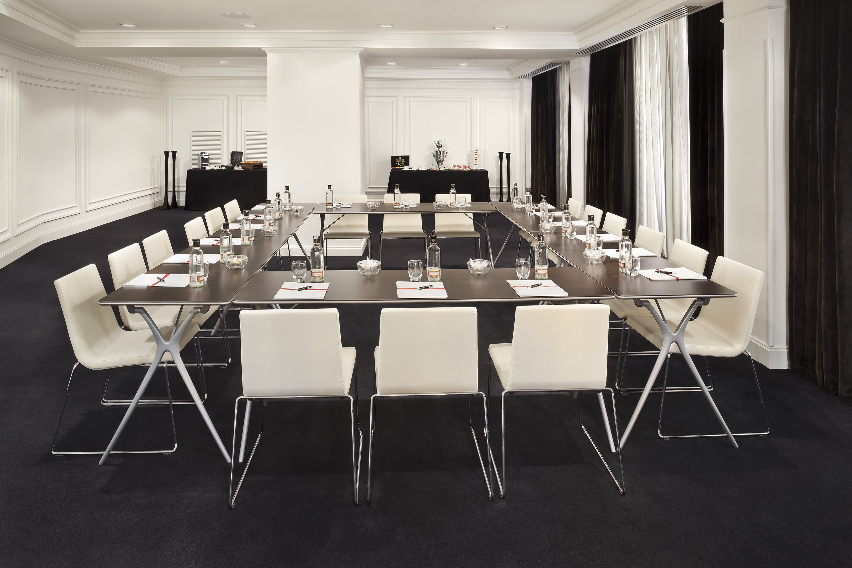 Modern meeting room with U-shaped table, white chairs, and refreshments setup.