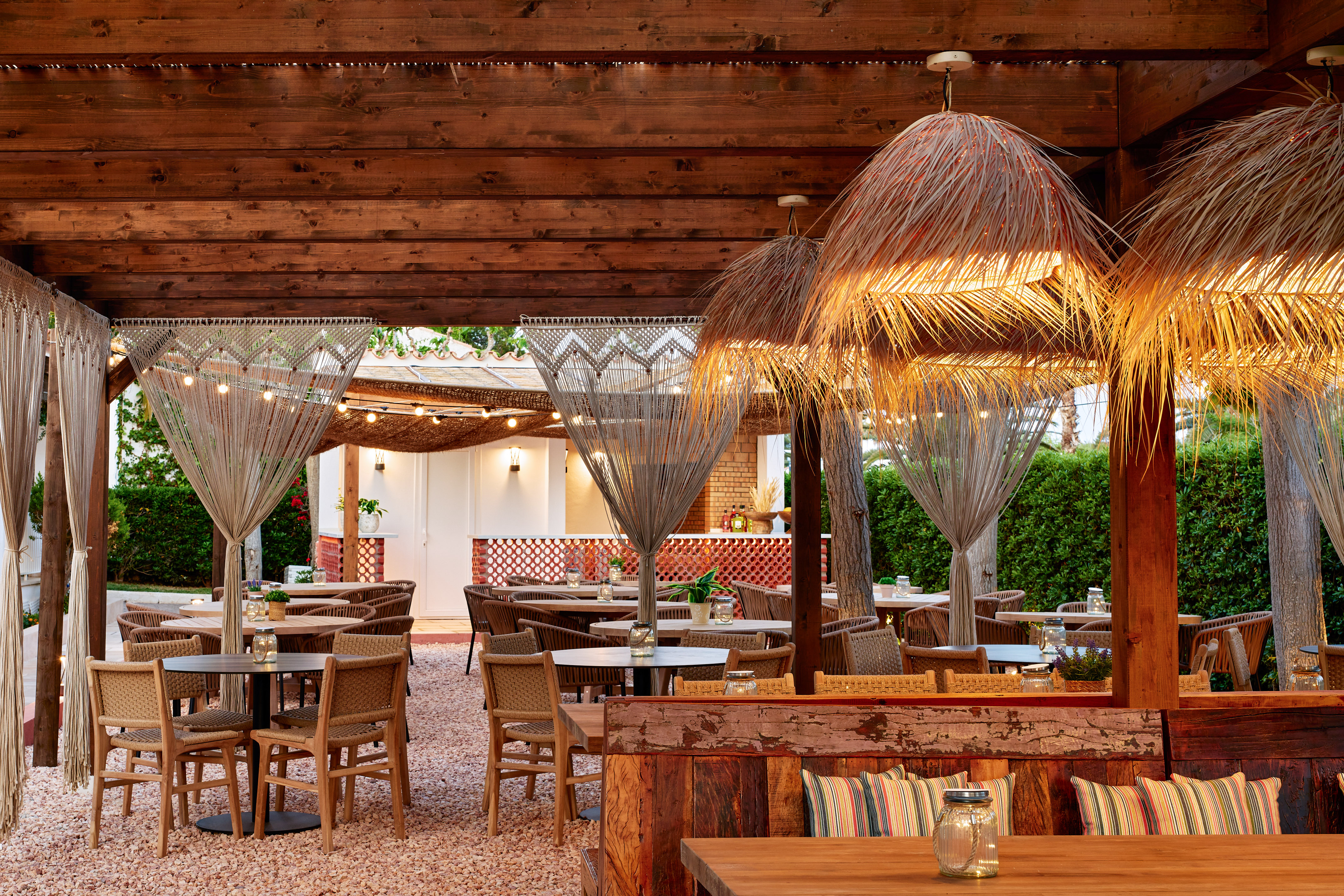 Al fresco dining patio with wooden pergola, straw lamps, and wicker chairs.