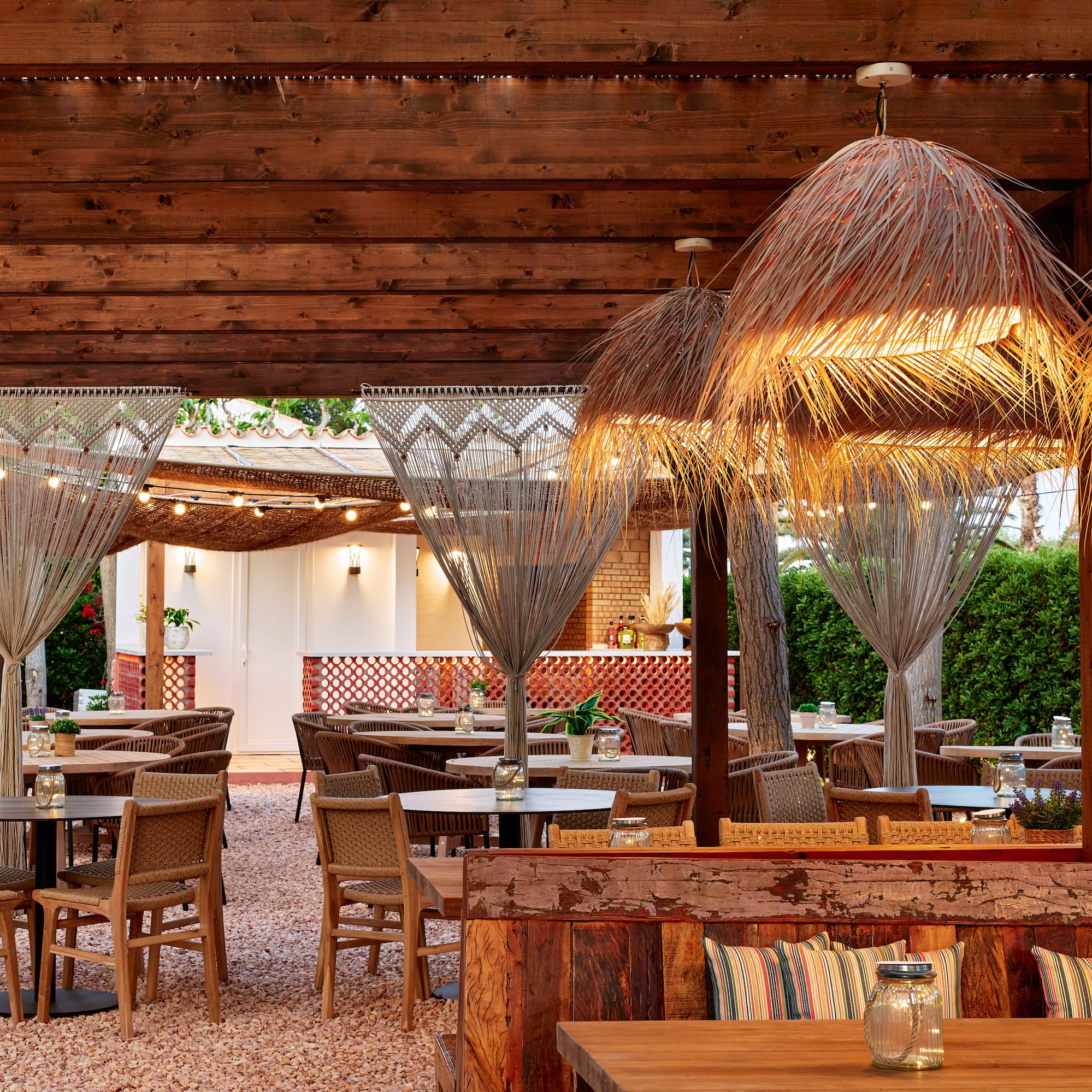 Al fresco dining patio with wooden pergola, straw lamps, and wicker chairs.