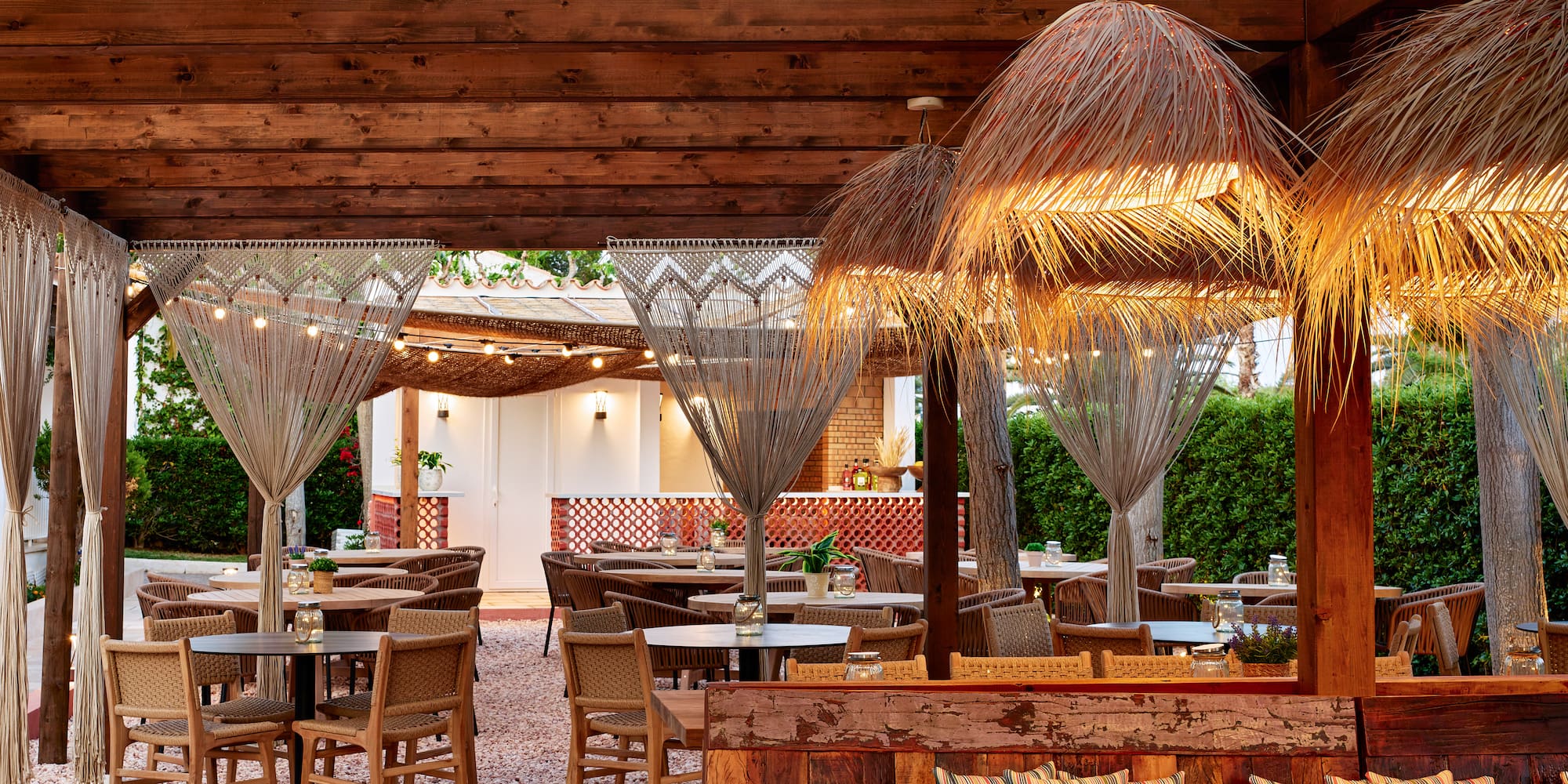 Al fresco dining patio with wooden pergola, straw lamps, and wicker chairs.