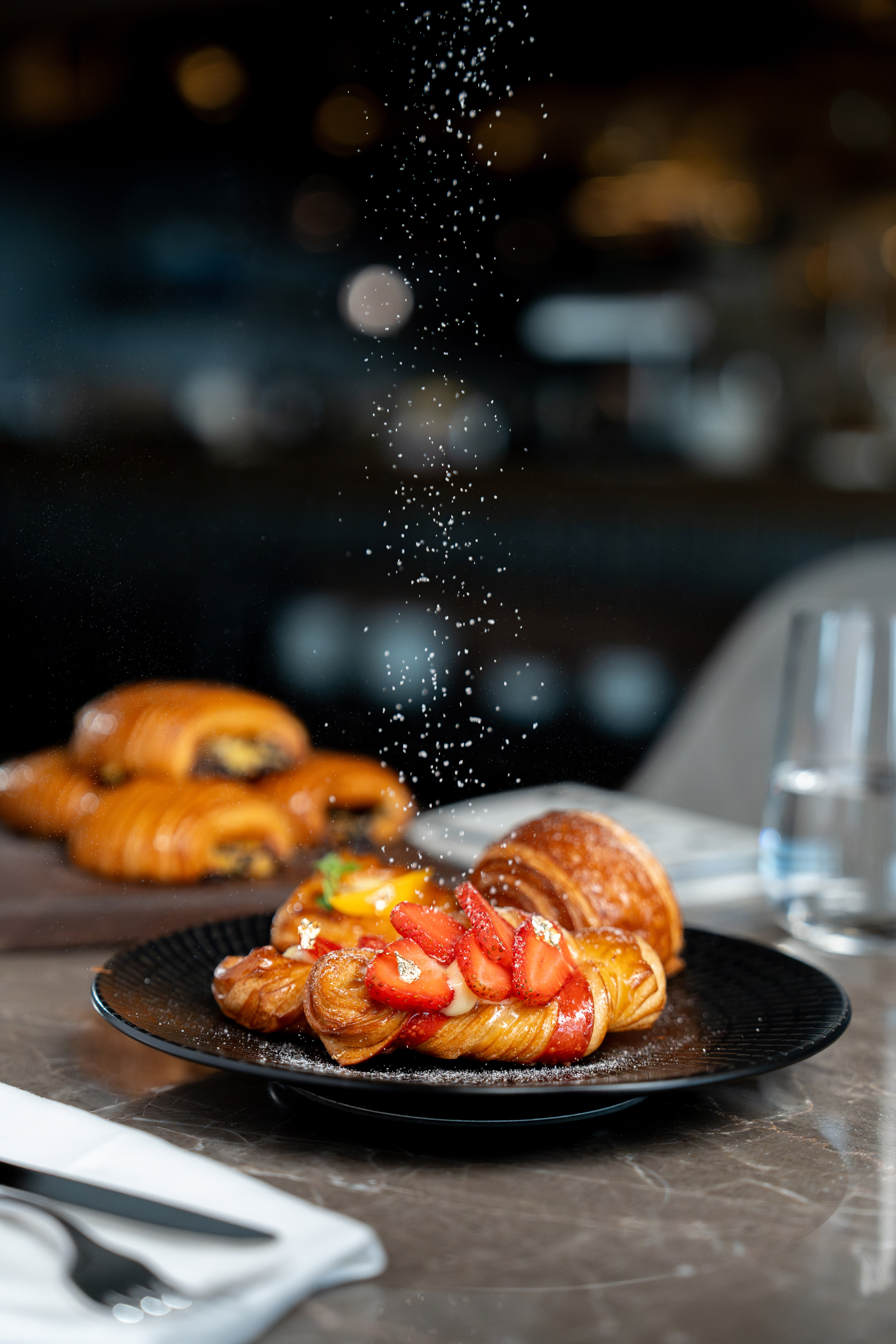 Powdered sugar on strawberry danish with cream and gold flakes.