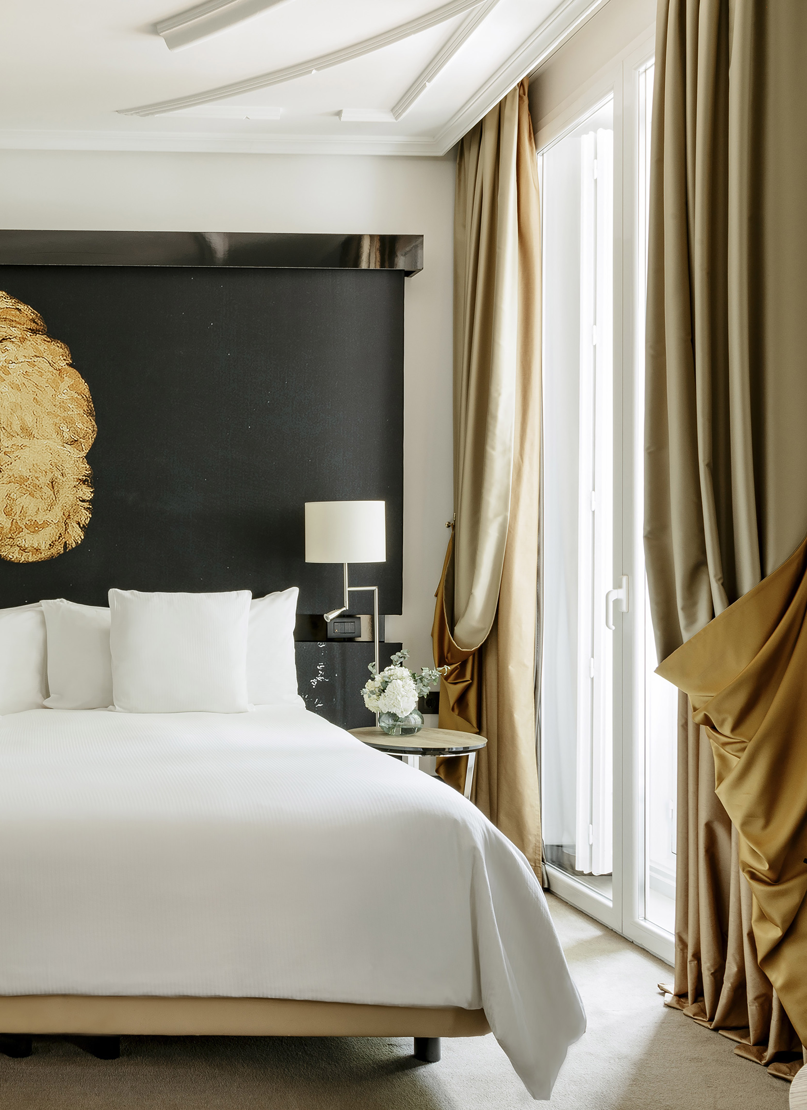 Luxurious hotel bedroom with white bed, black headboard, and golden curtains.