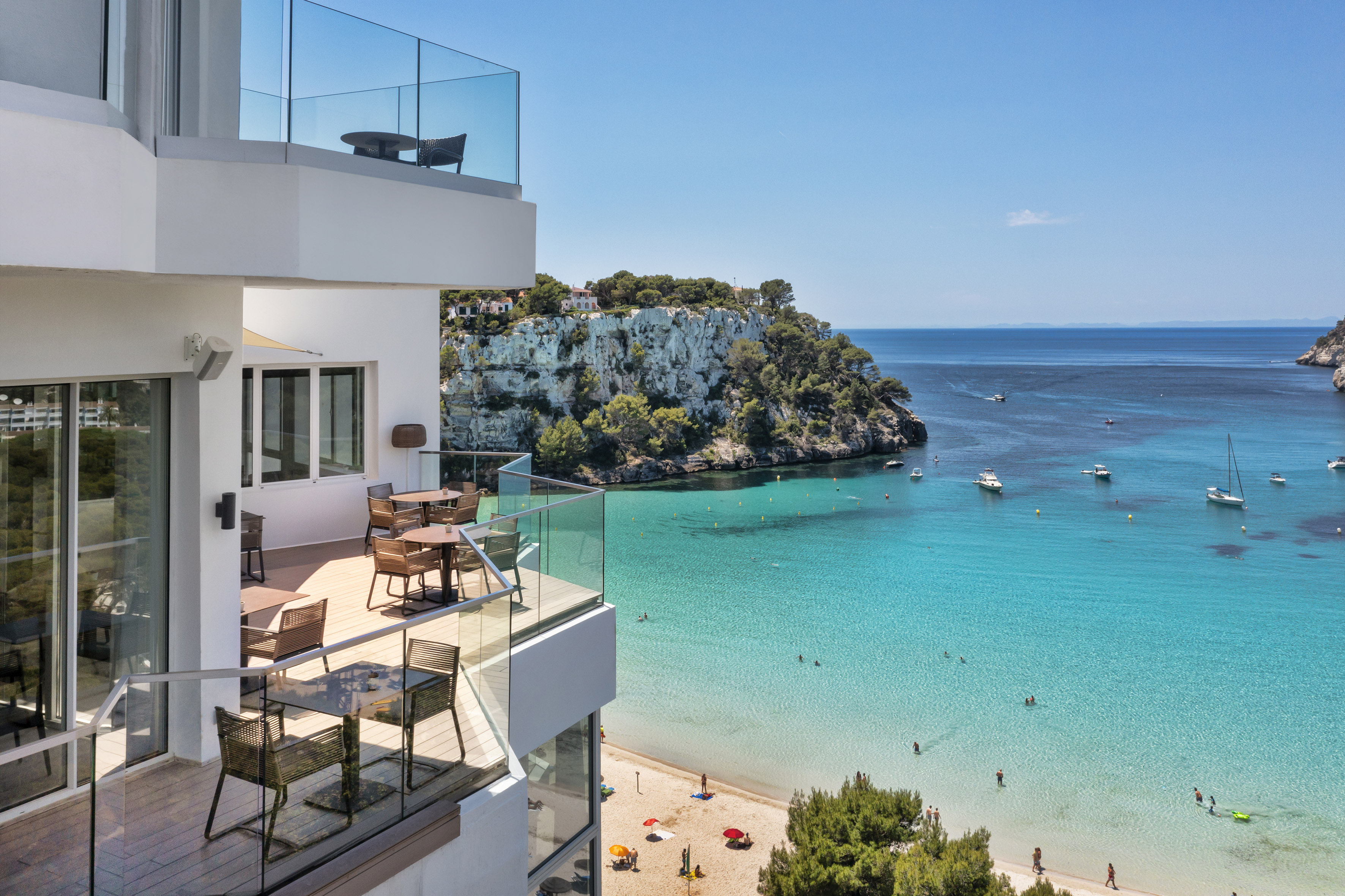 Hotel balcony overlooking turquoise bay, sandy beach, and cliffs.
