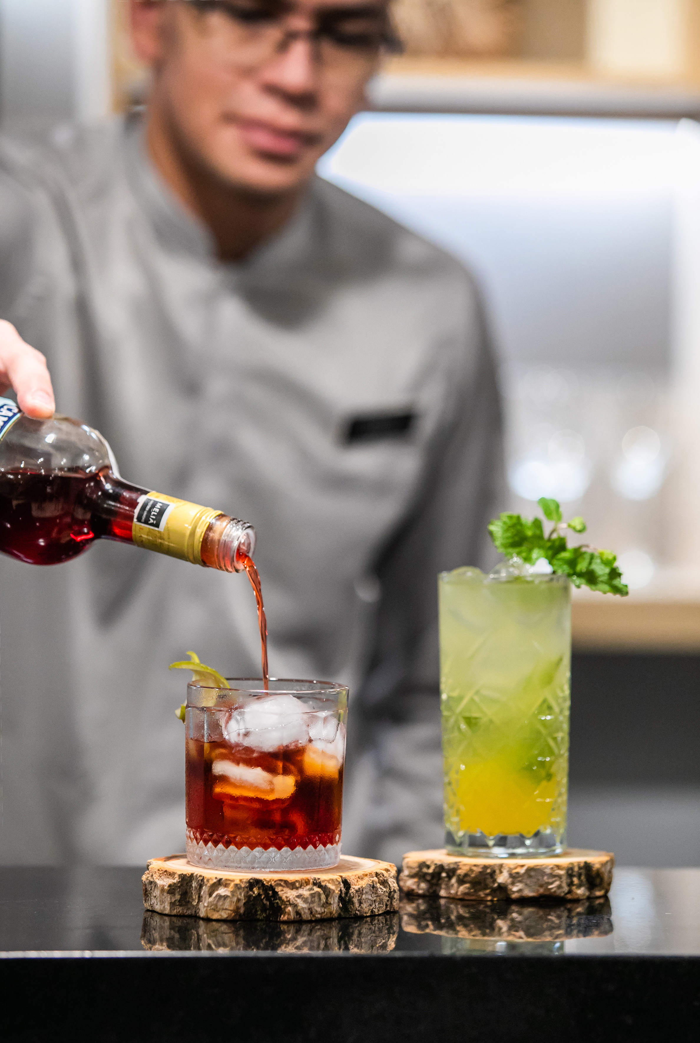 Bartender pouring red cocktail into glass; fresh green cocktail with mint.