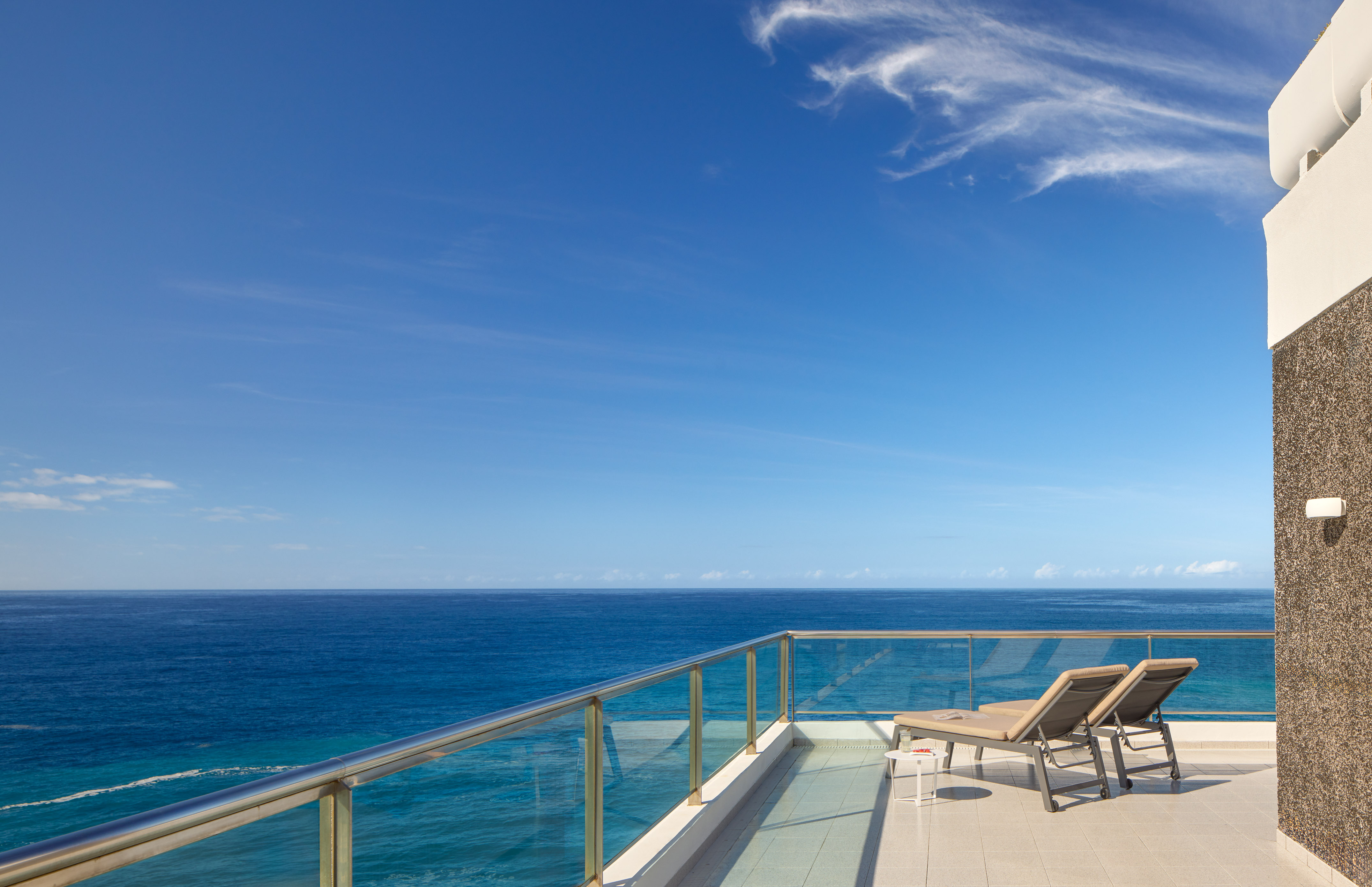 Resort balcony with lounge chairs, clear blue ocean view.