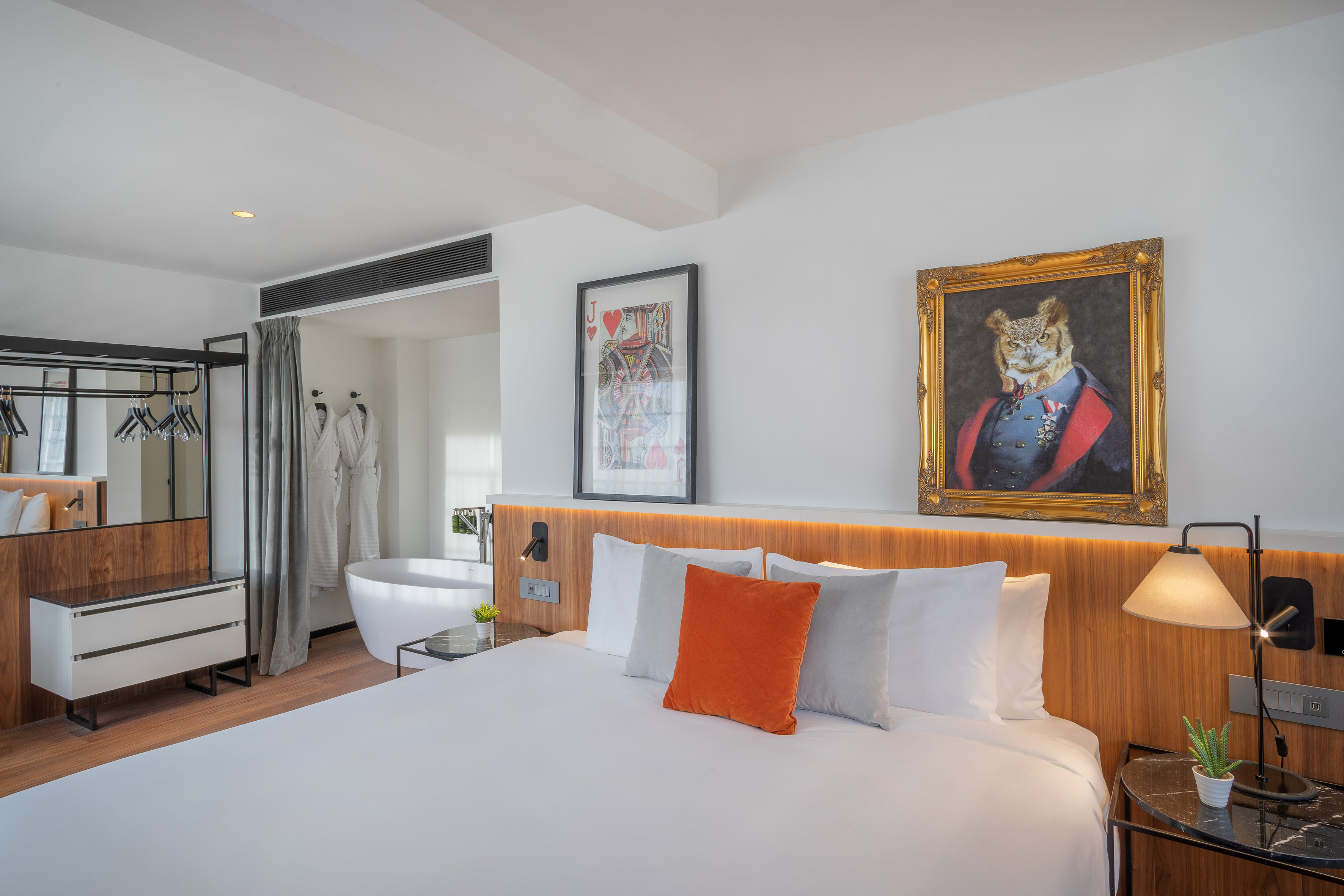 Open-plan hotel room with king bed, freestanding tub, and quirky wall art.