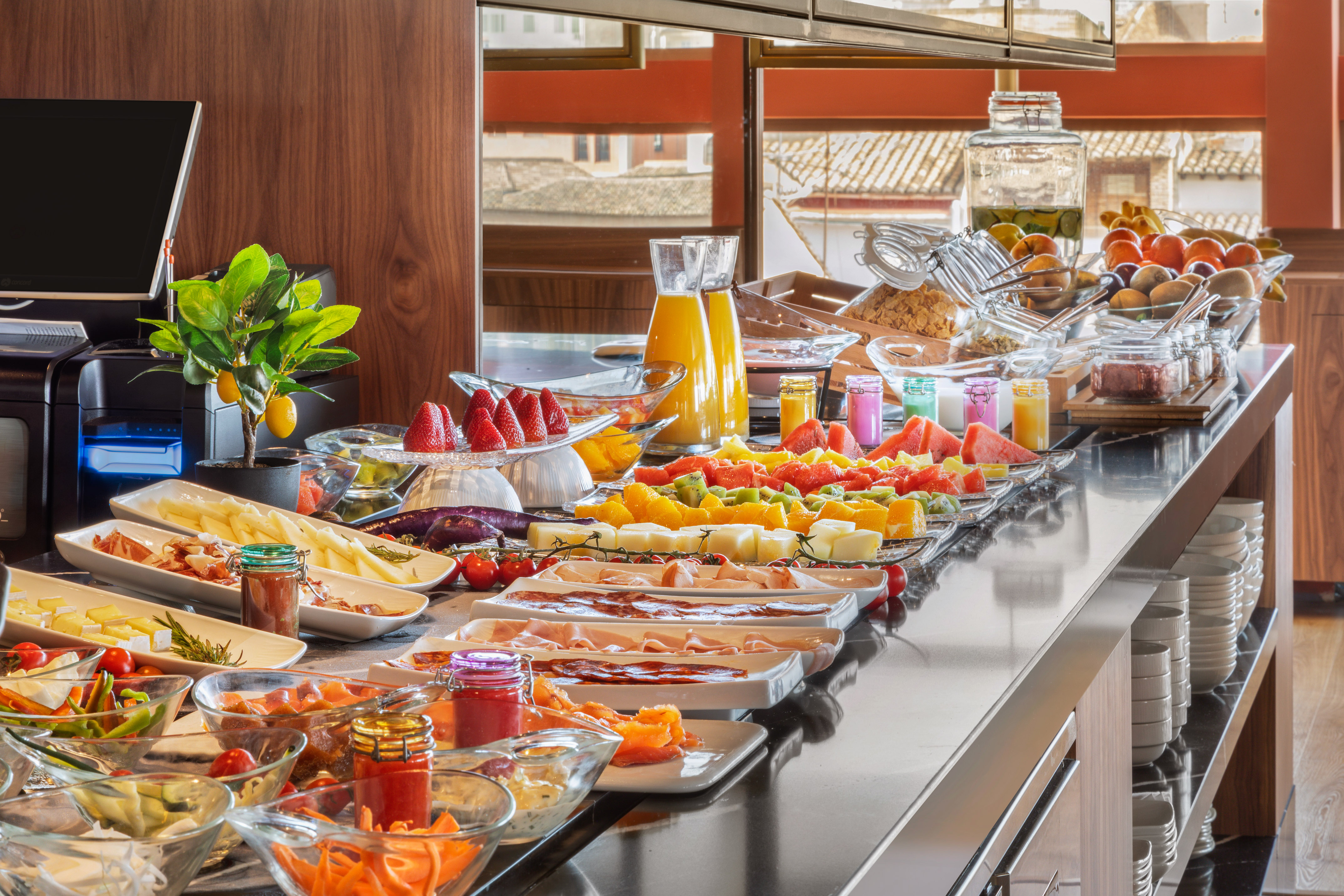 Hotel breakfast buffet with fresh fruit, cheeses, cold cuts, and juices.