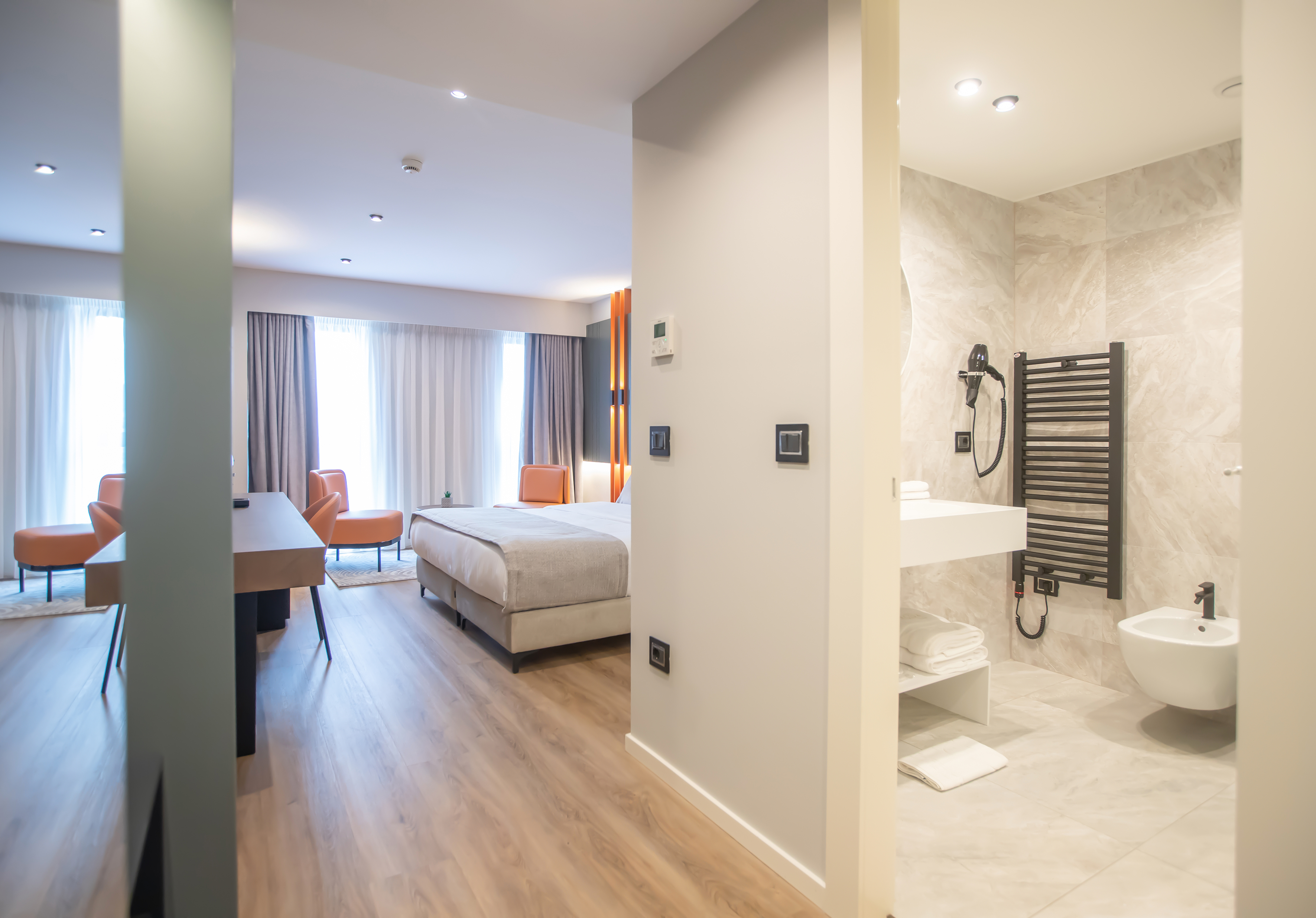 Modern hotel room with bed, orange chairs, and sleek bathroom view.