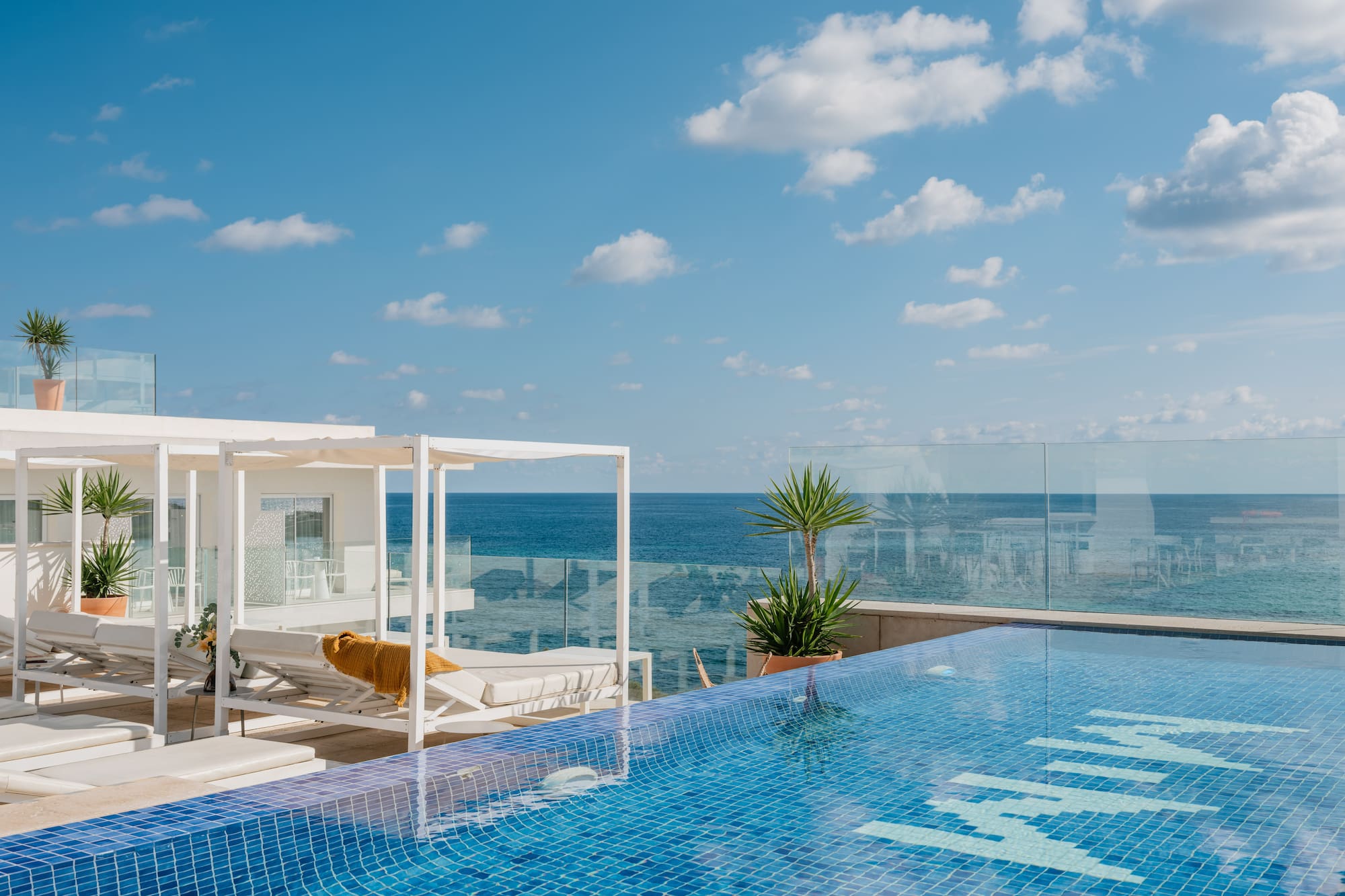 a pool with a deck chair and a glass railing overlooking the ocean