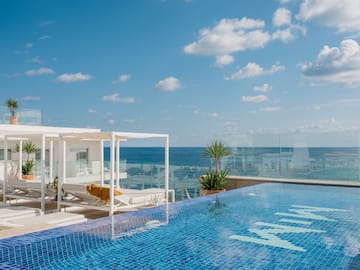 a pool with a deck chair and a glass railing overlooking the ocean
