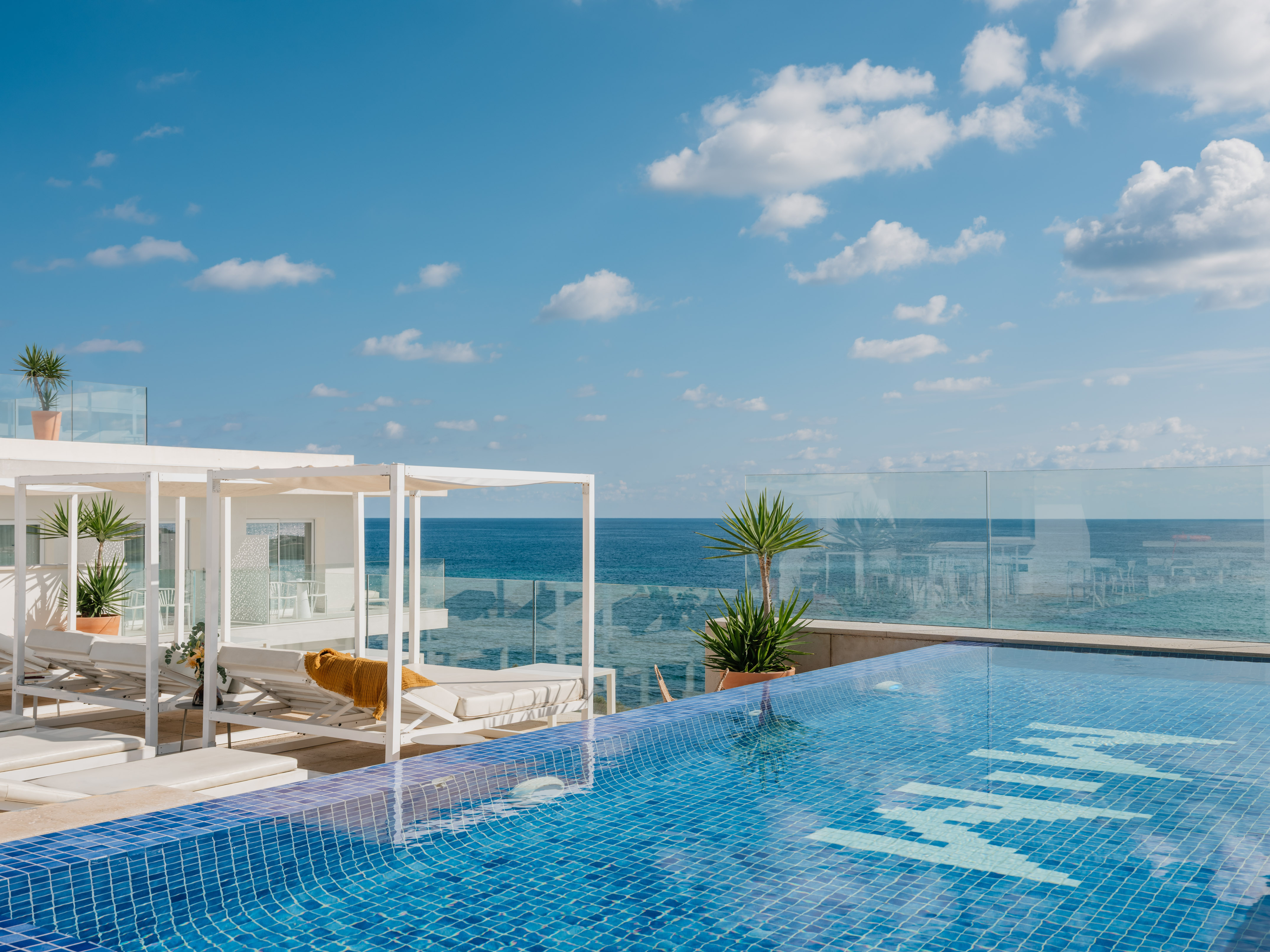 Oceanfront infinity pool with white cabanas, ocean view, and blue sky.