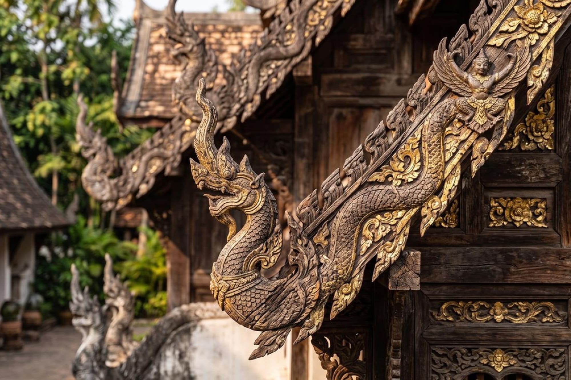 Ornate wooden Naga and Garuda carvings with gold details on a Thai temple roof.