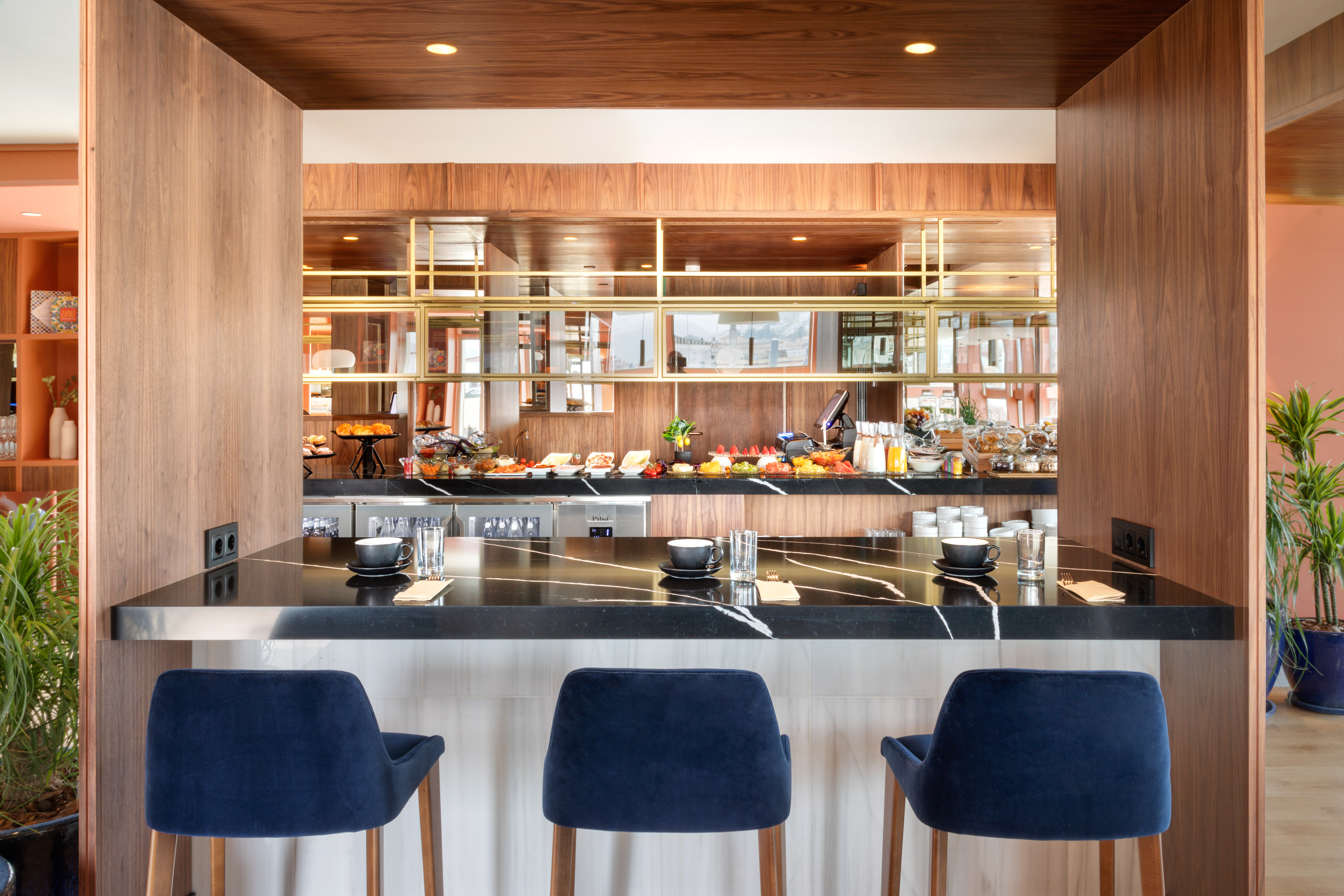 Hotel breakfast bar with marble counter, blue stools, and a full buffet.
