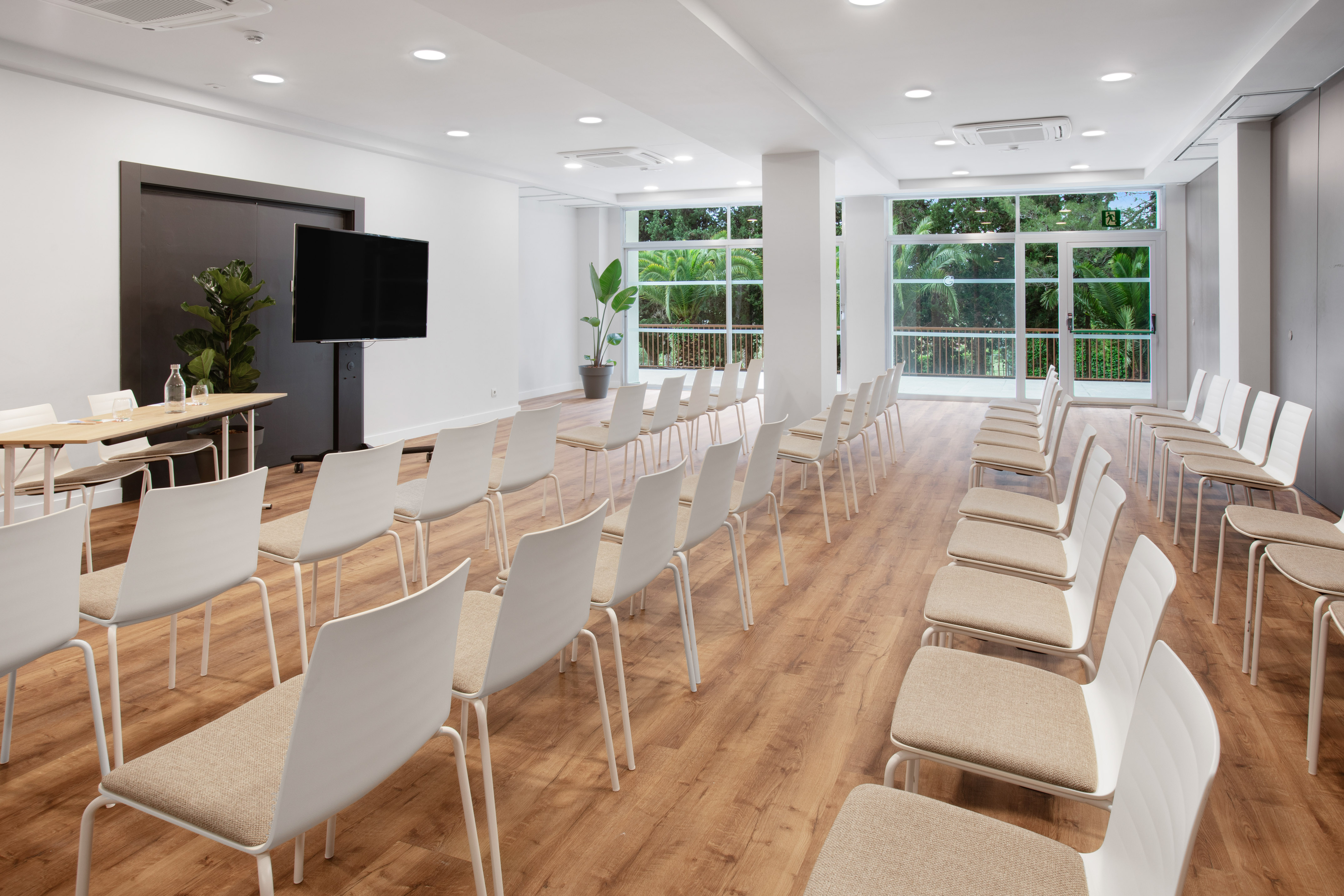 Bright conference room with seminar setup, TV, and lush tropical view.