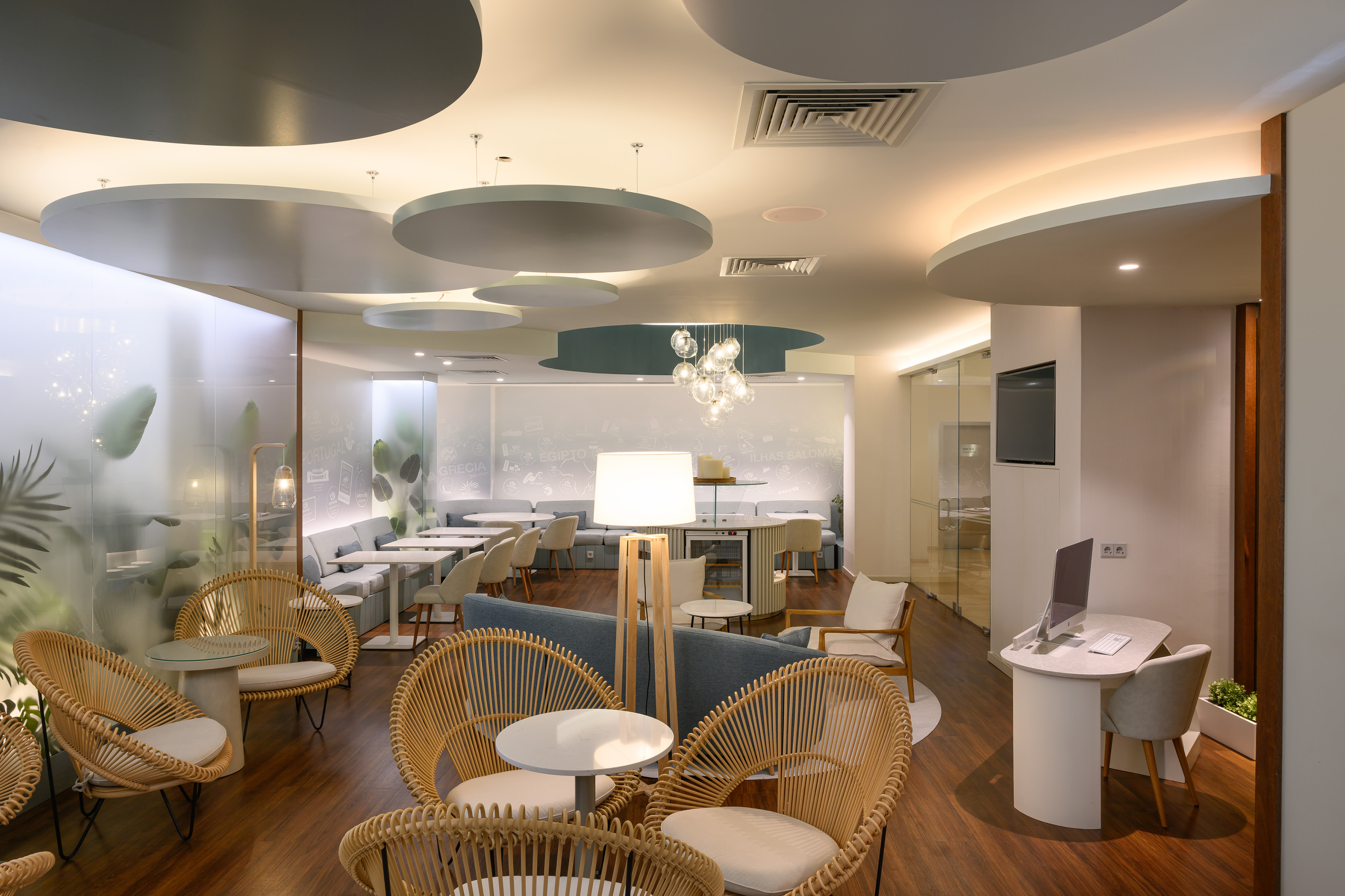 Modern lounge interior with rattan chairs, blue sofa, and curved ceiling lighting.
