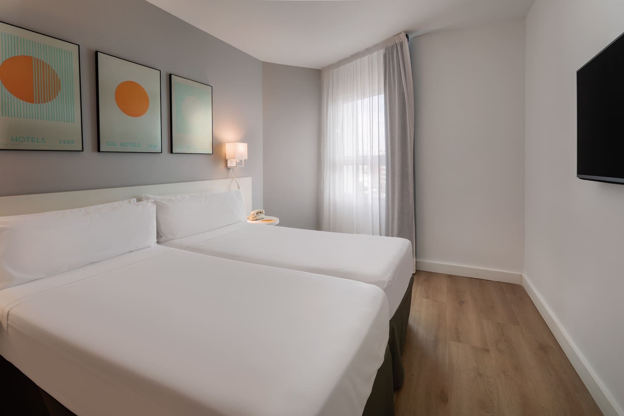 Sol Hotels twin bedroom with white beds, wooden floor, wall art, window, and TV.