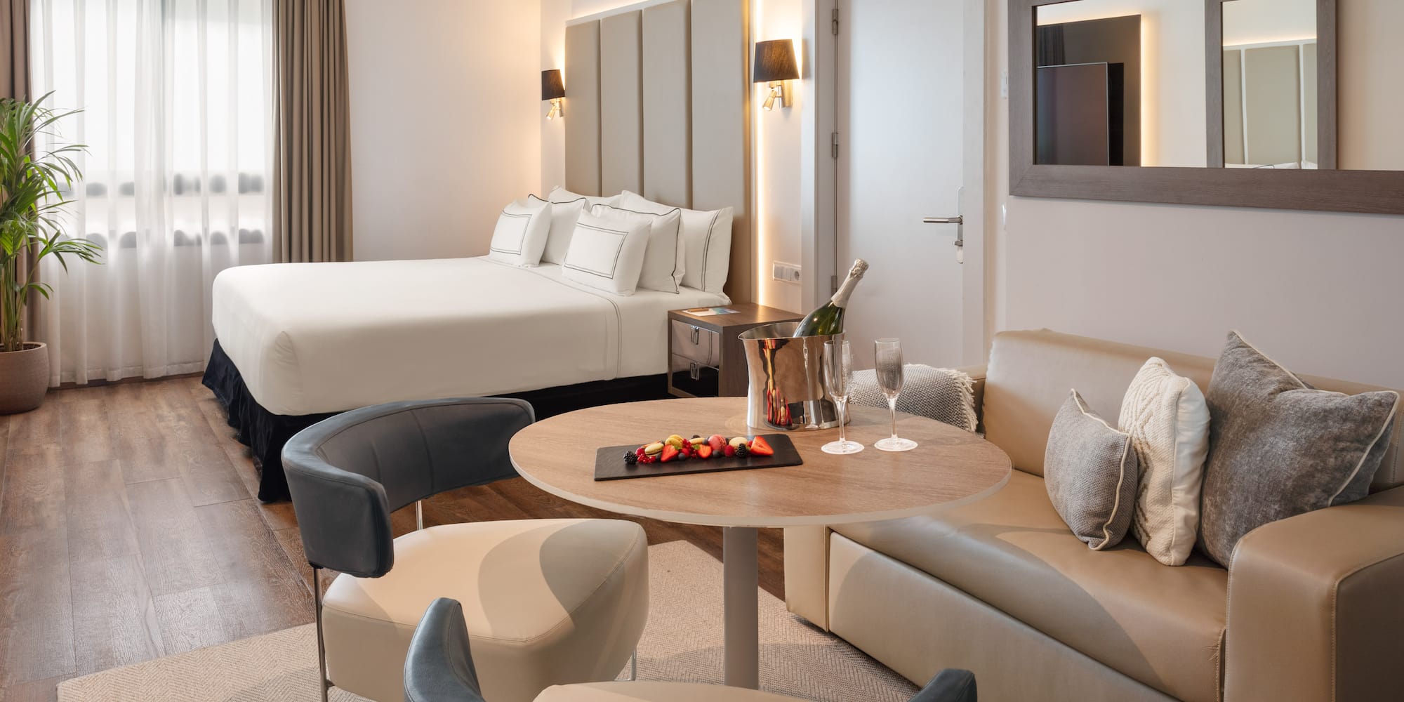 Luxury hotel suite with king bed, lounge area, champagne, and fruit.
