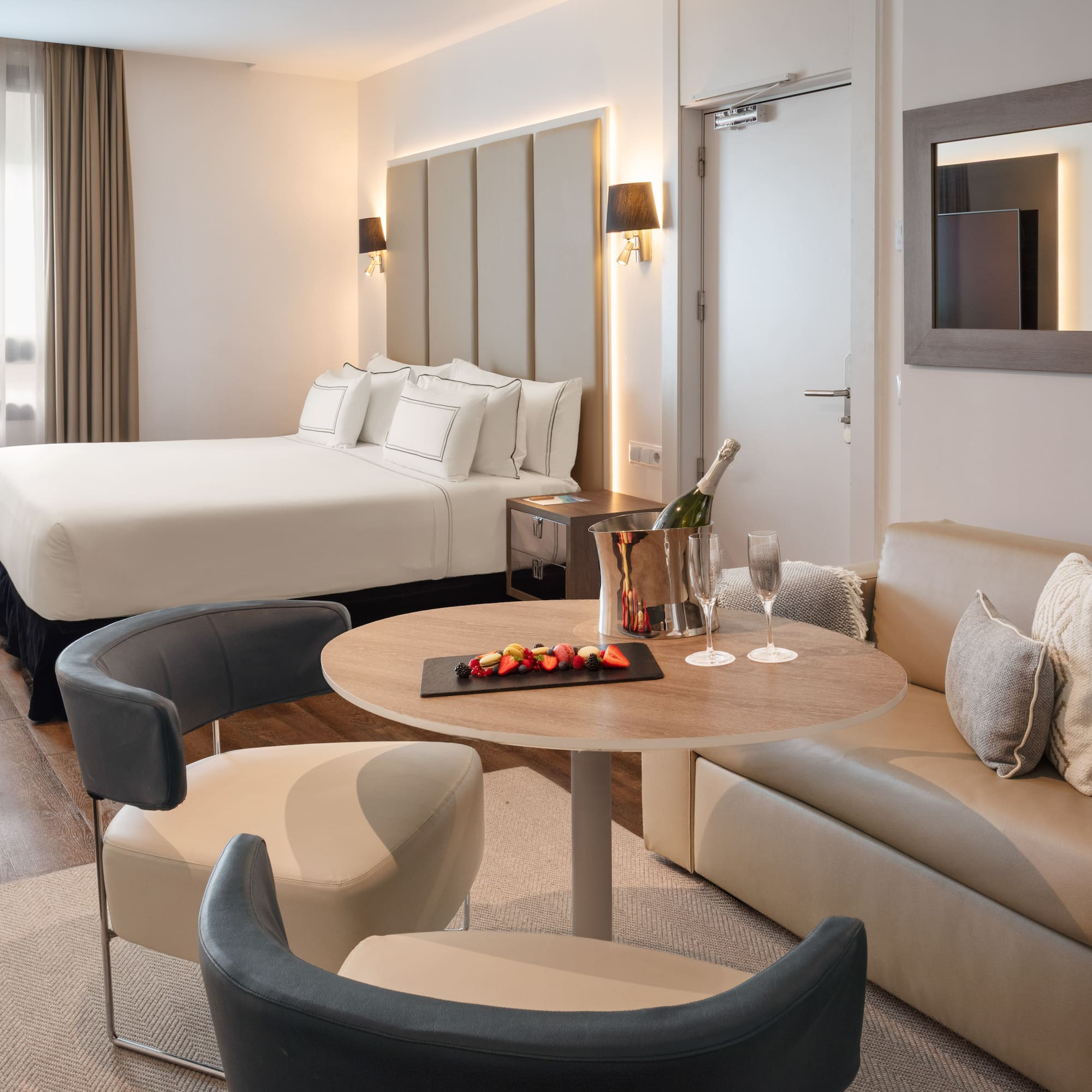 Luxury hotel suite with king bed, lounge area, champagne, and fruit.