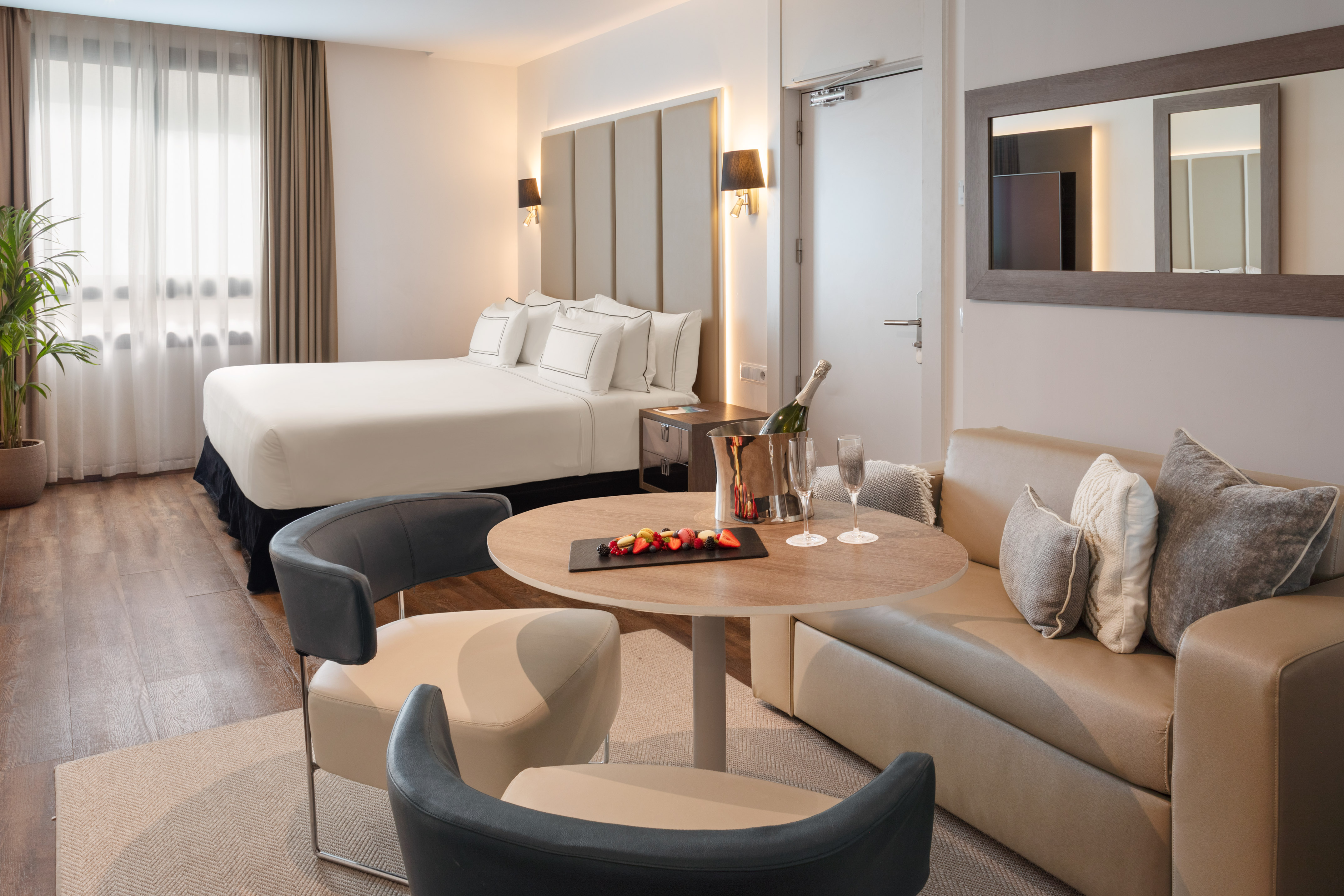 Luxury hotel suite with king bed, lounge area, champagne, and fruit.