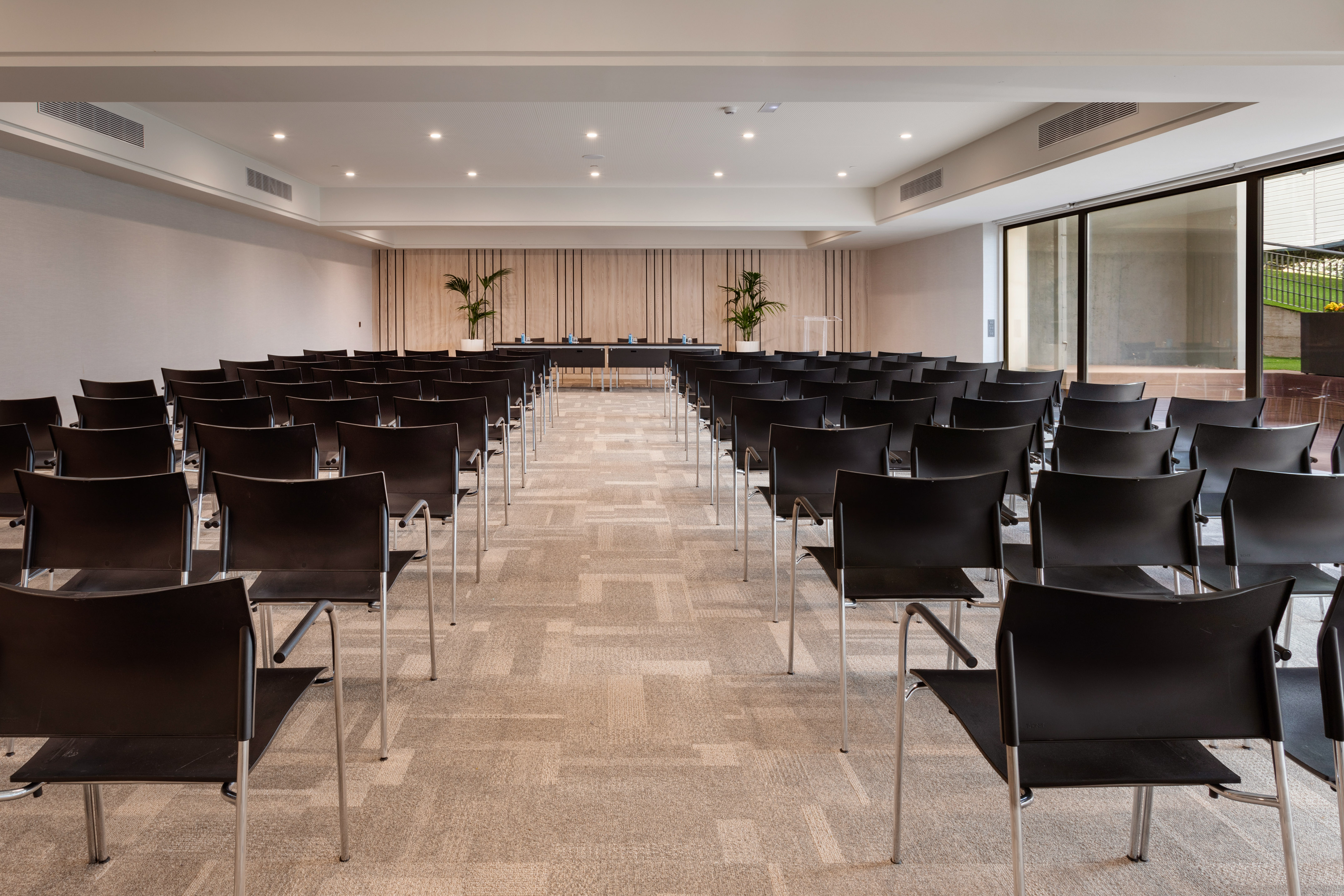 Modern conference room with black chairs in rows, front table, and natural light.
