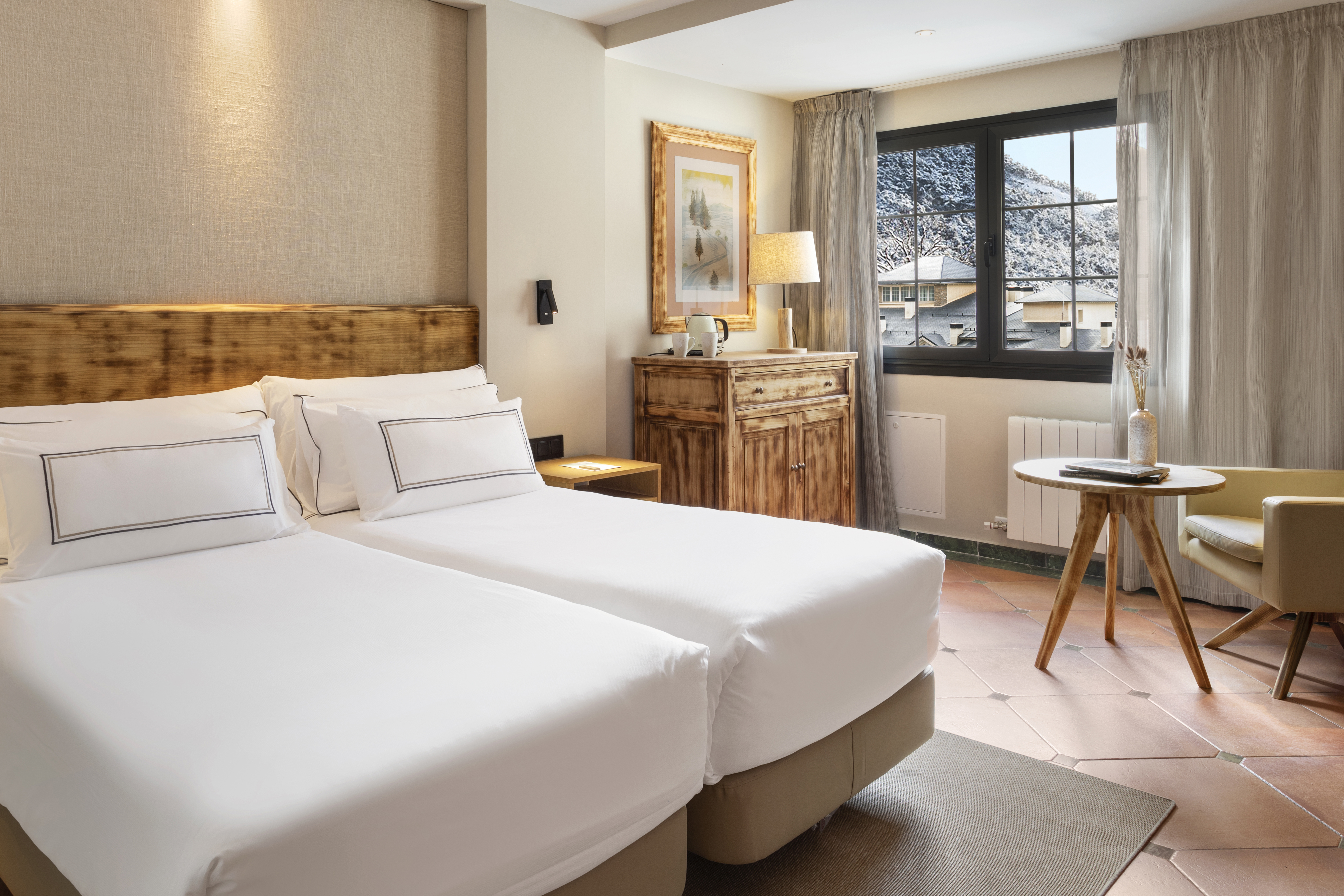 Hotel room with twin beds, wooden furnishings, and snowy mountain view.
