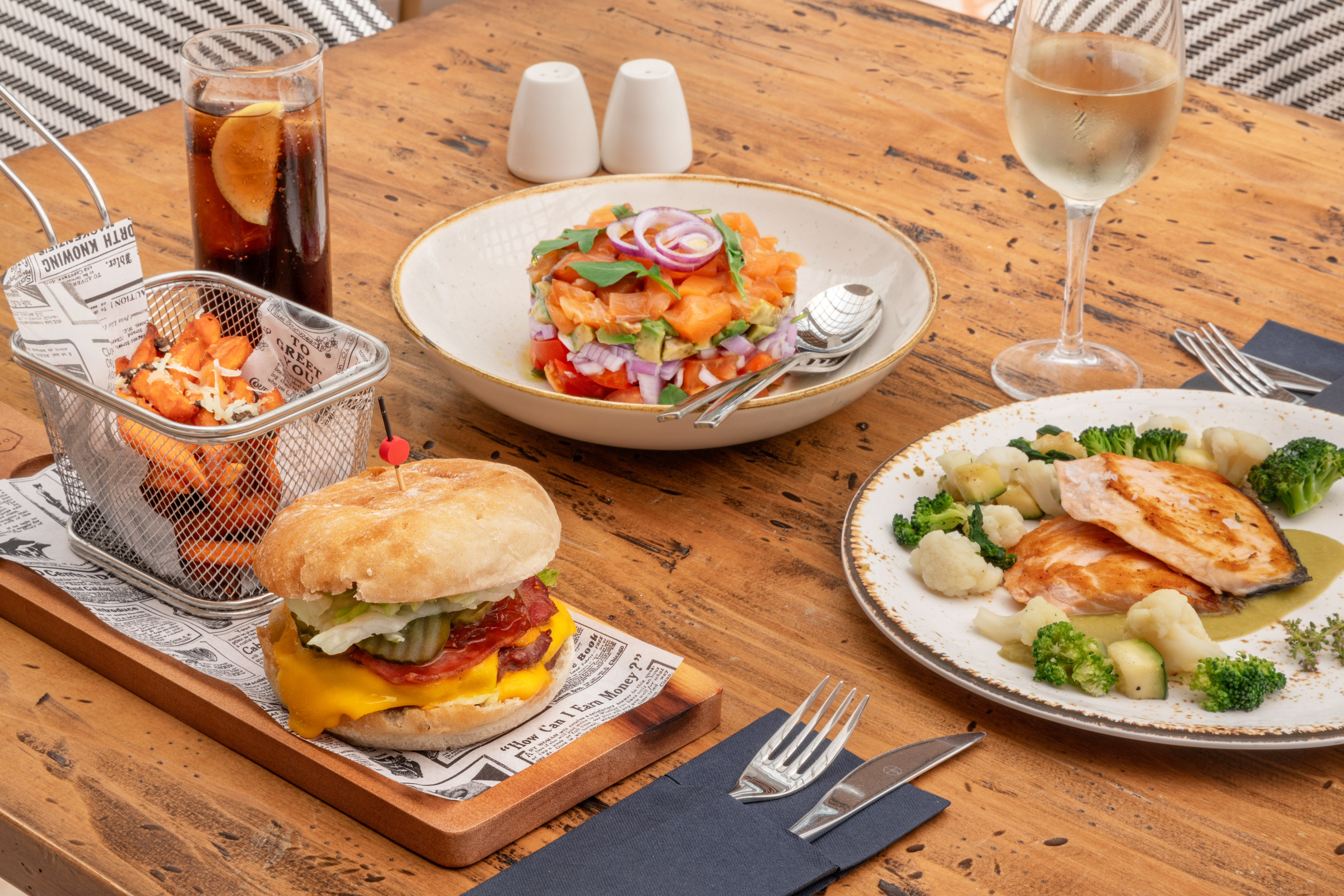 Cheeseburger, sweet potato fries, salmon salad, grilled salmon, and wine on table.