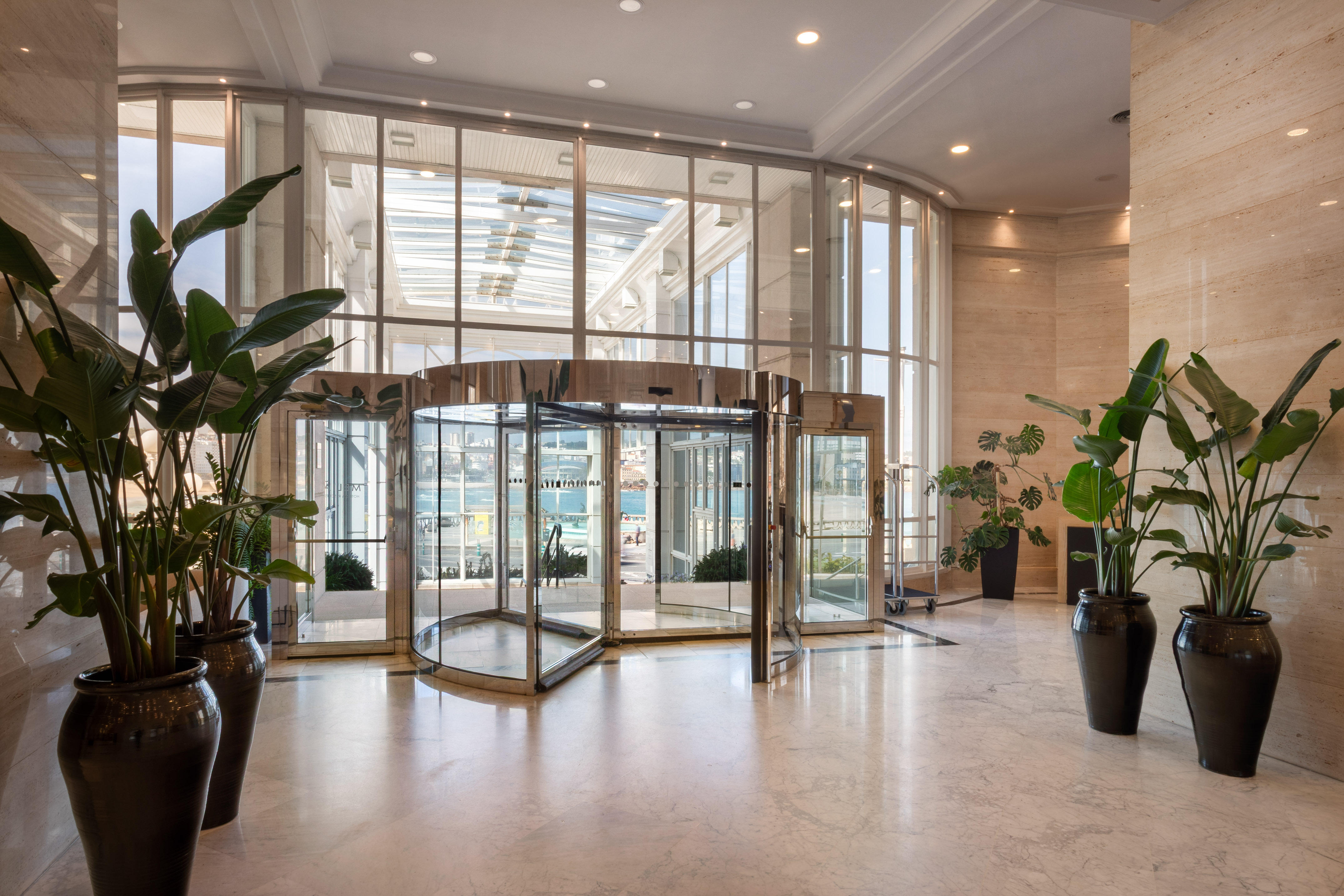 Bright, modern hotel lobby with revolving glass doors and potted plants.