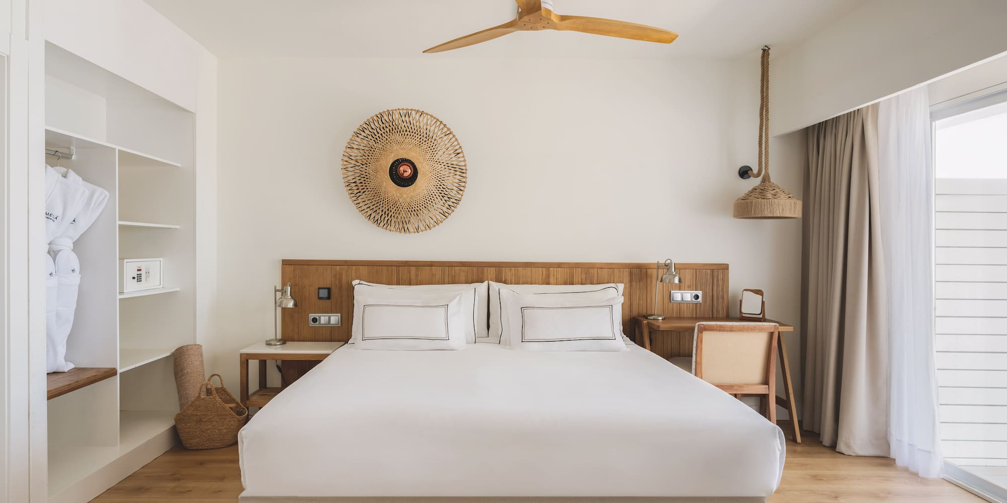 Hotel bedroom with king bed, wooden accents, closet, ceiling fan, and natural decor.