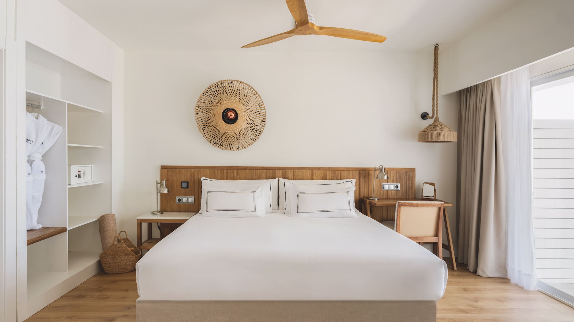 Hotel bedroom with king bed, wooden accents, closet, ceiling fan, and natural decor.