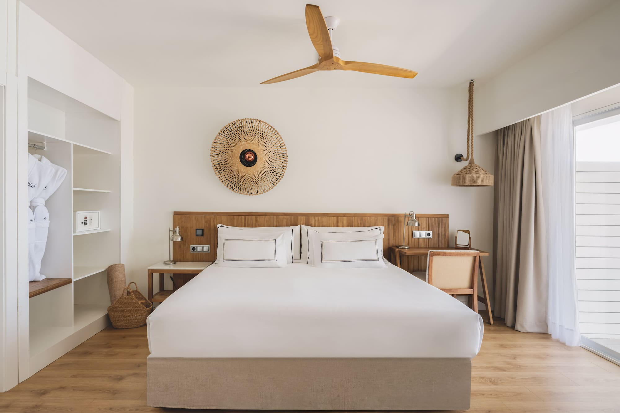 Hotel bedroom with king bed, wooden accents, closet, ceiling fan, and natural decor.