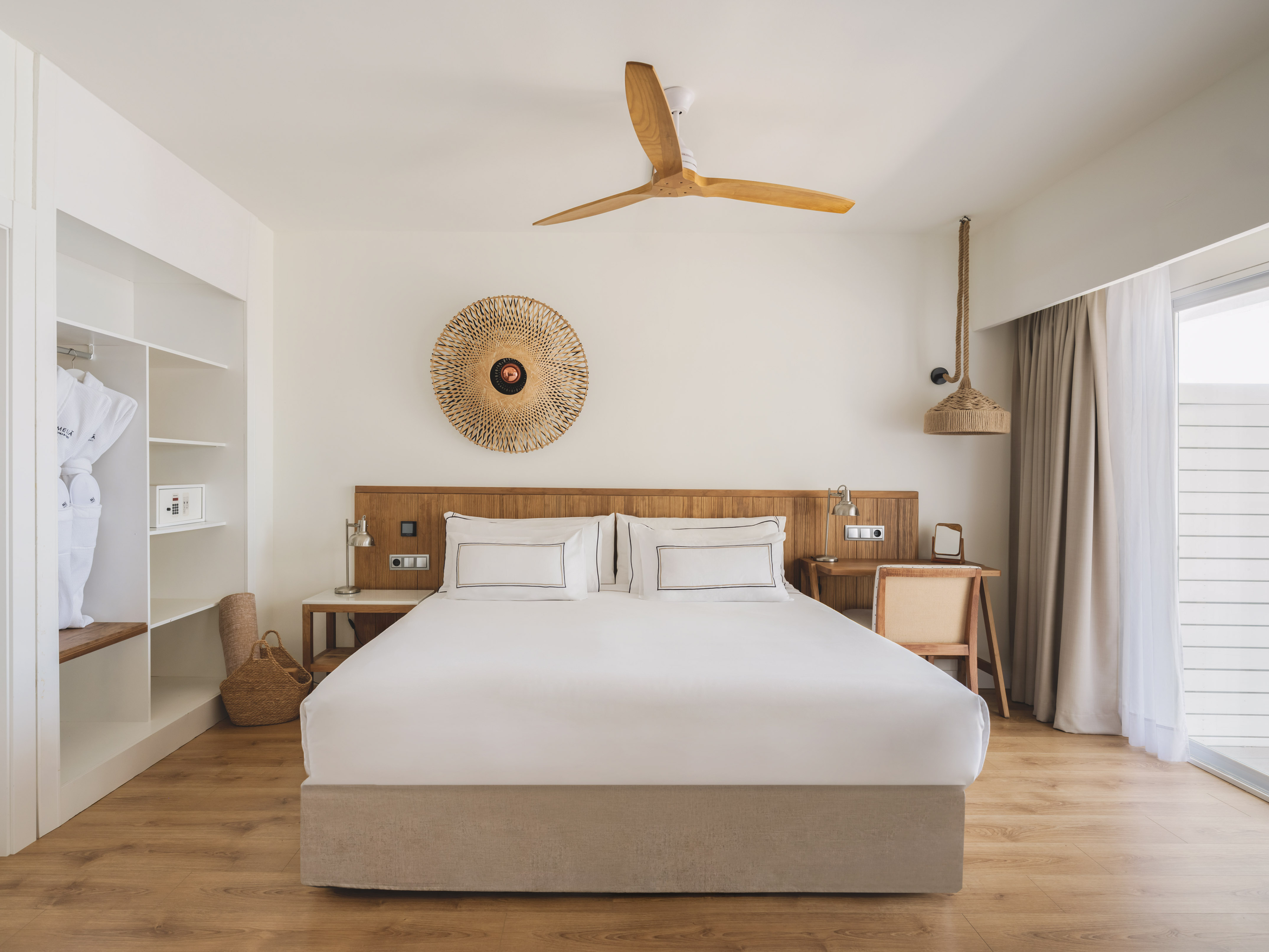 Hotel bedroom with king bed, wooden accents, closet, ceiling fan, and natural decor.