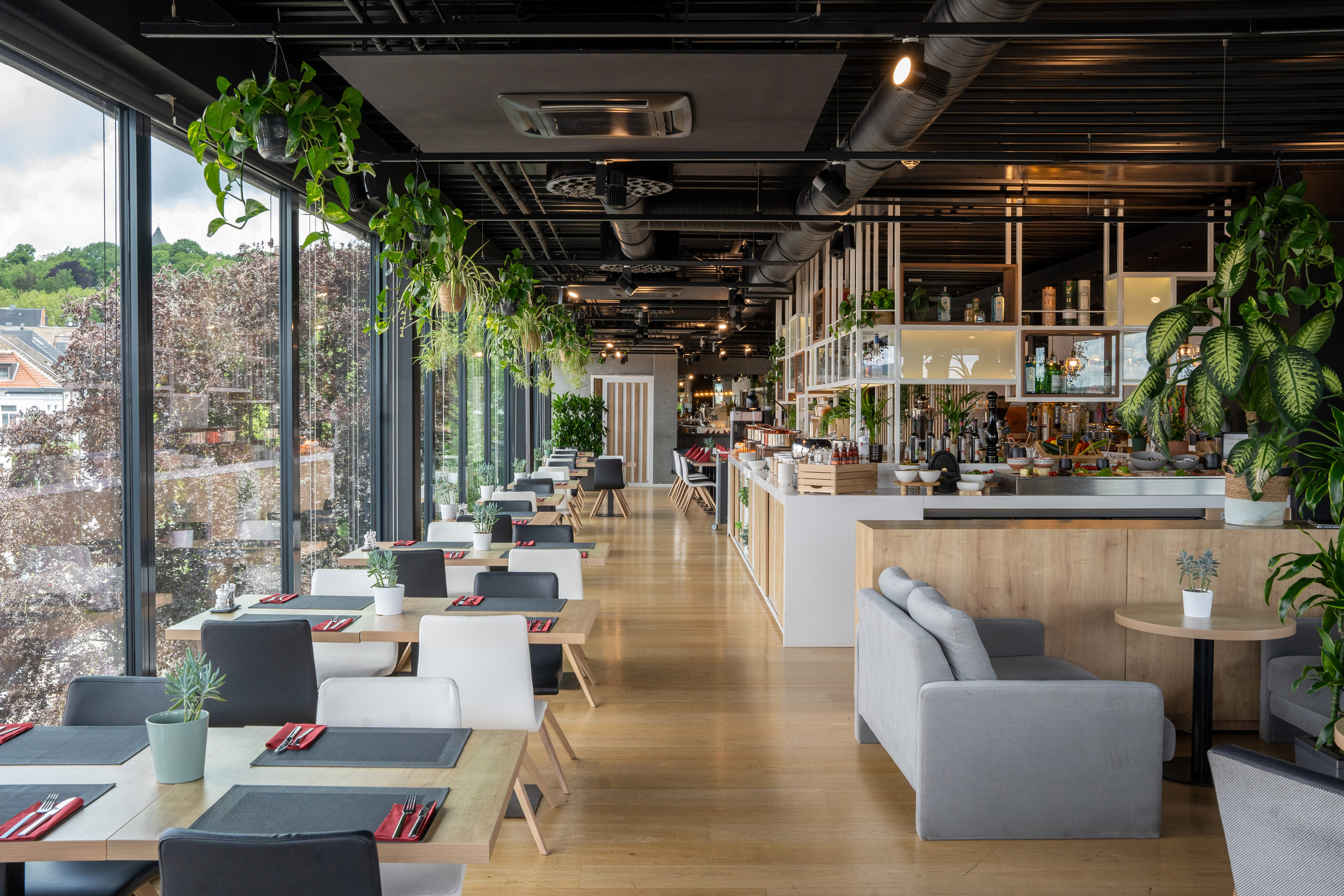 Modern restaurant dining with large windows, buffet, and abundant plants.
