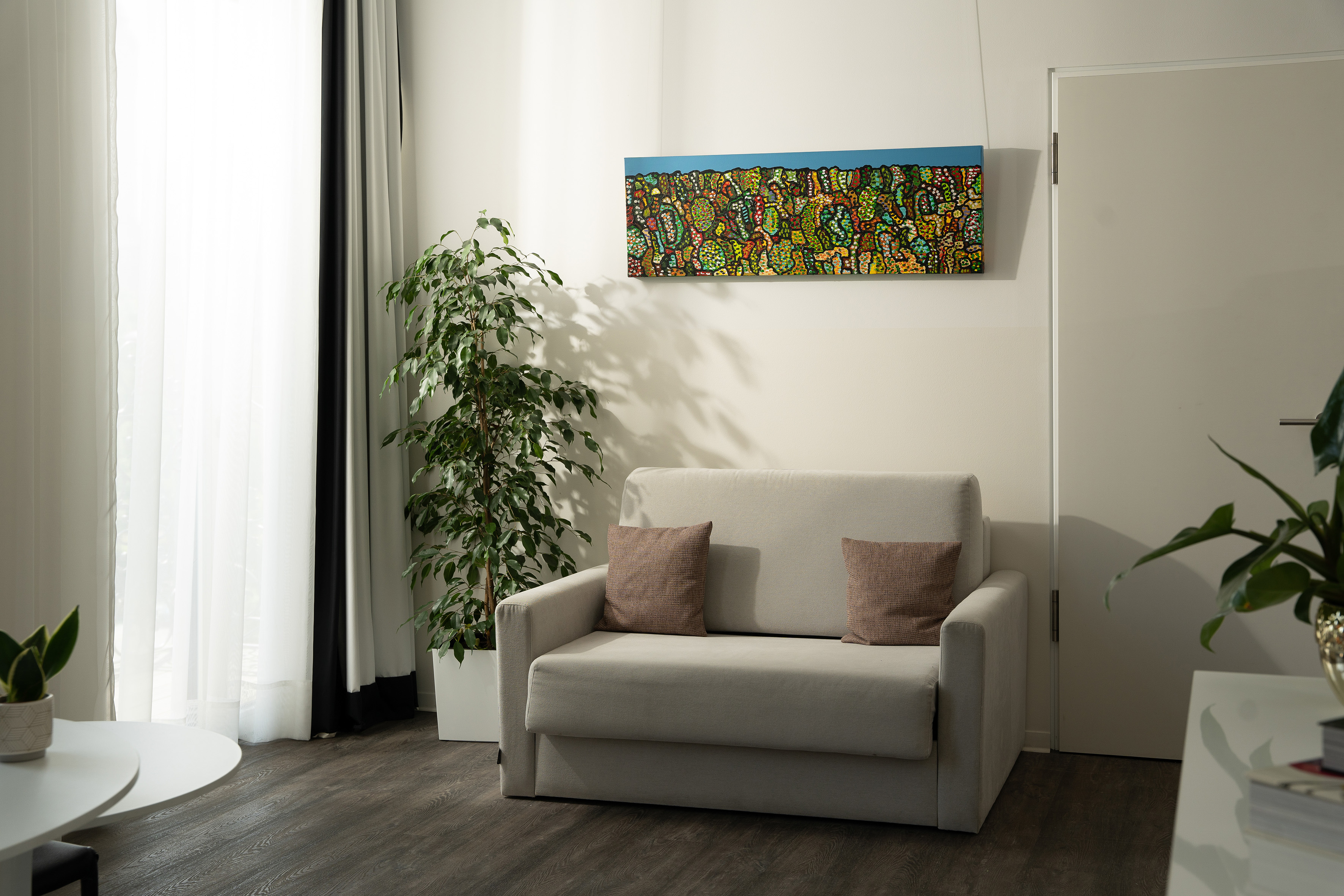 Modern living room with grey sofa, colorful abstract painting, and tall ficus plant.