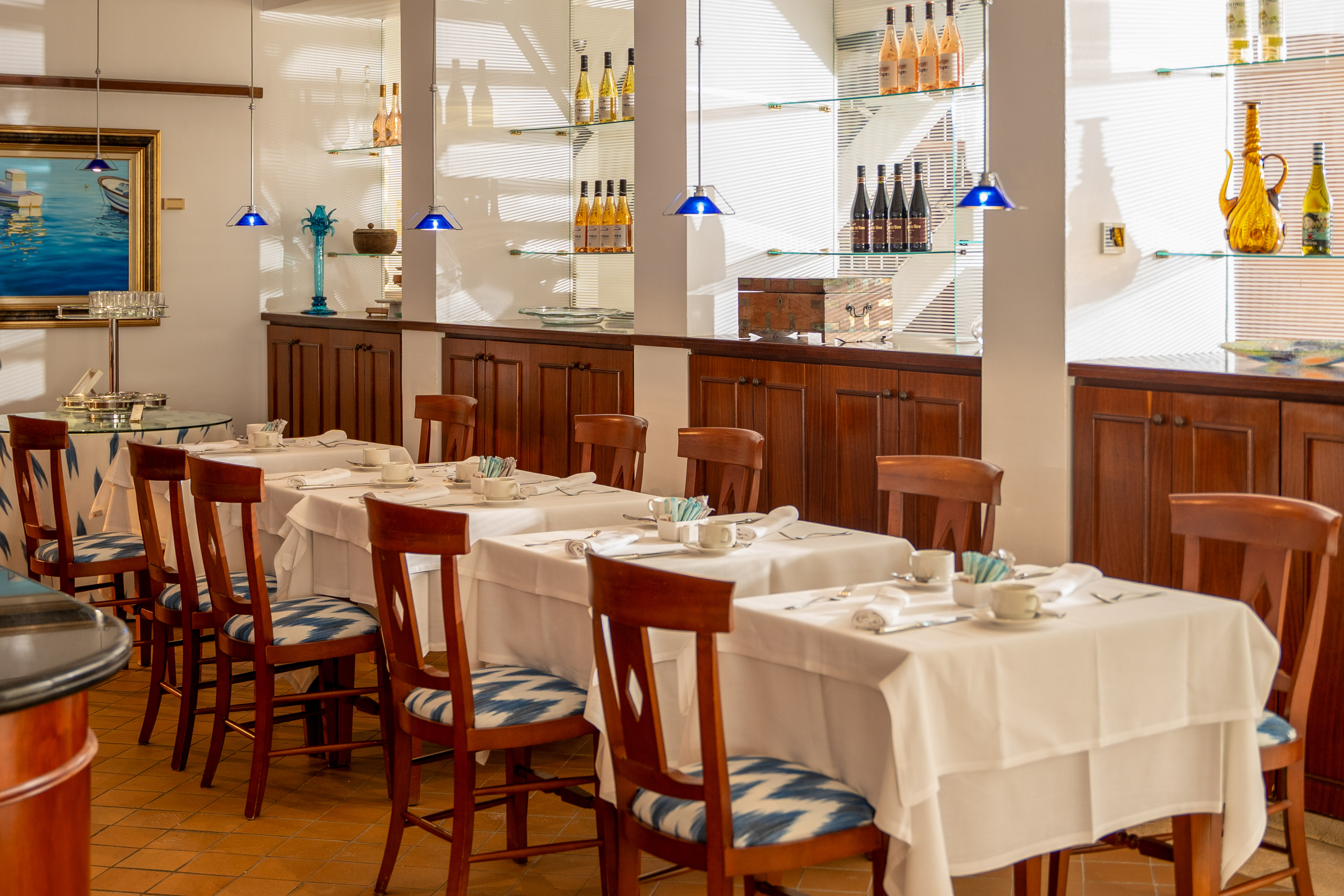 Elegant restaurant dining room with set tables, blue patterned chairs, and display shelves.