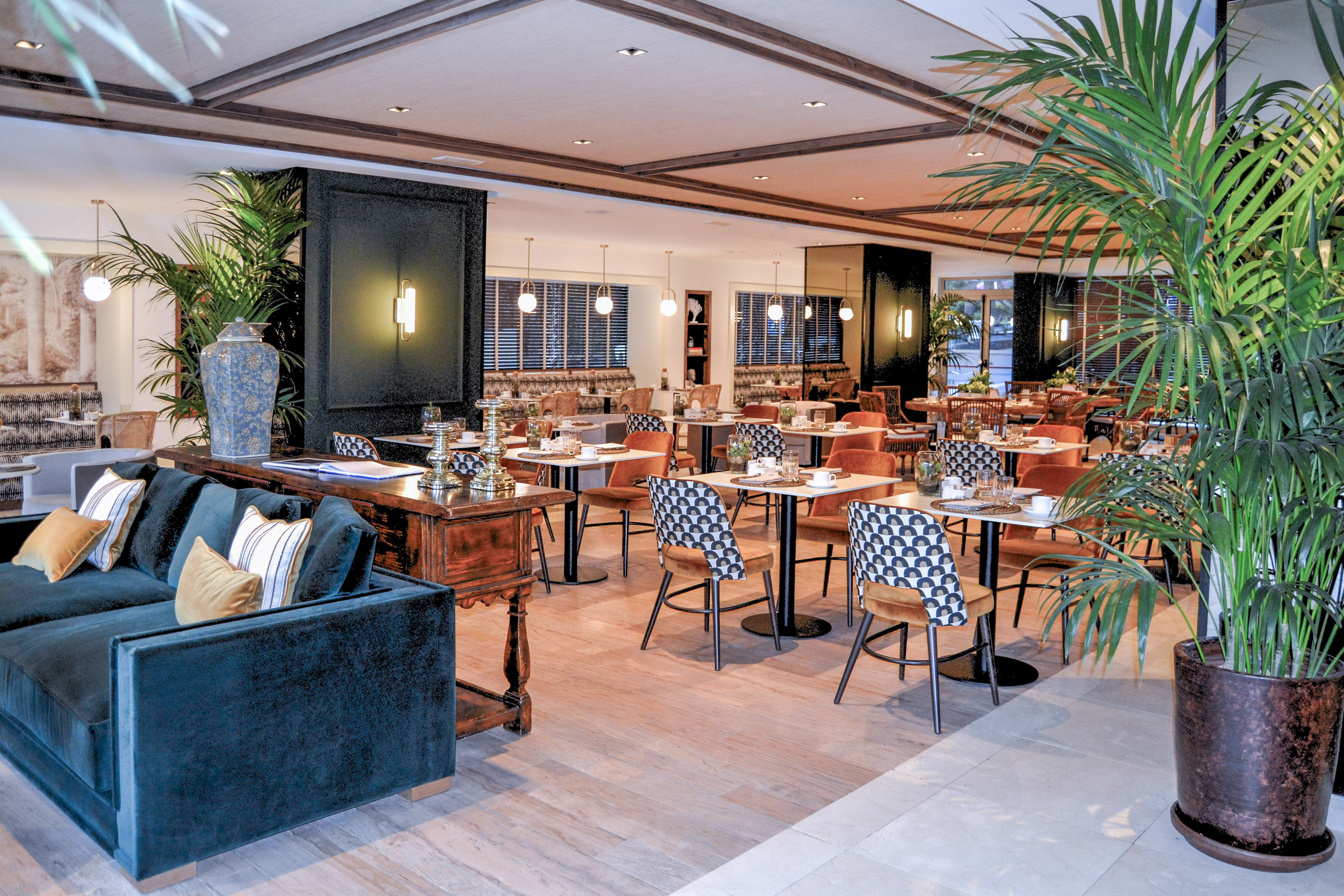 Elegant restaurant interior with set dining tables, velvet sofa, and potted plants.