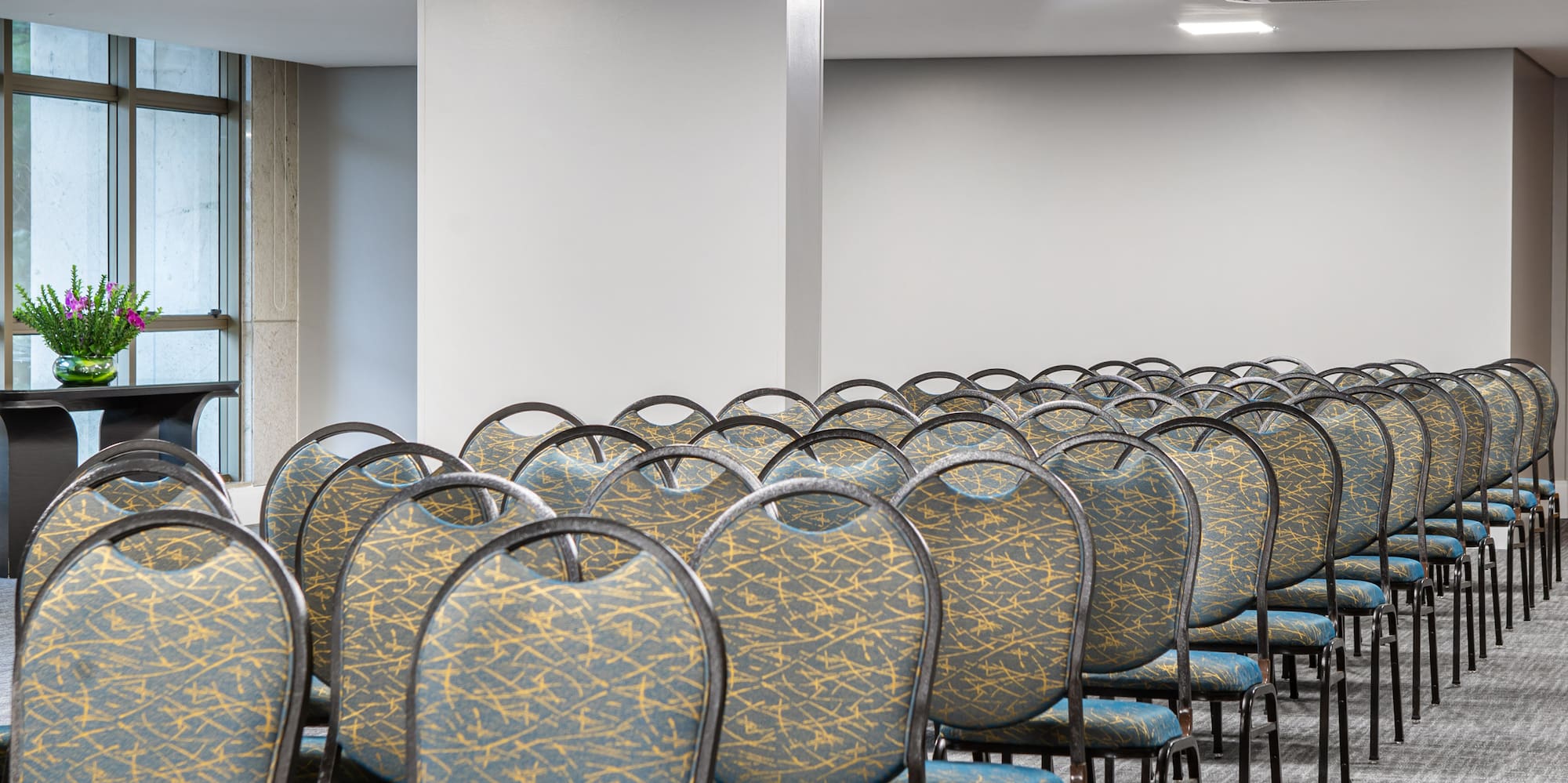 Empty conference room with rows of patterned chairs, grey carpet, and modern lights.